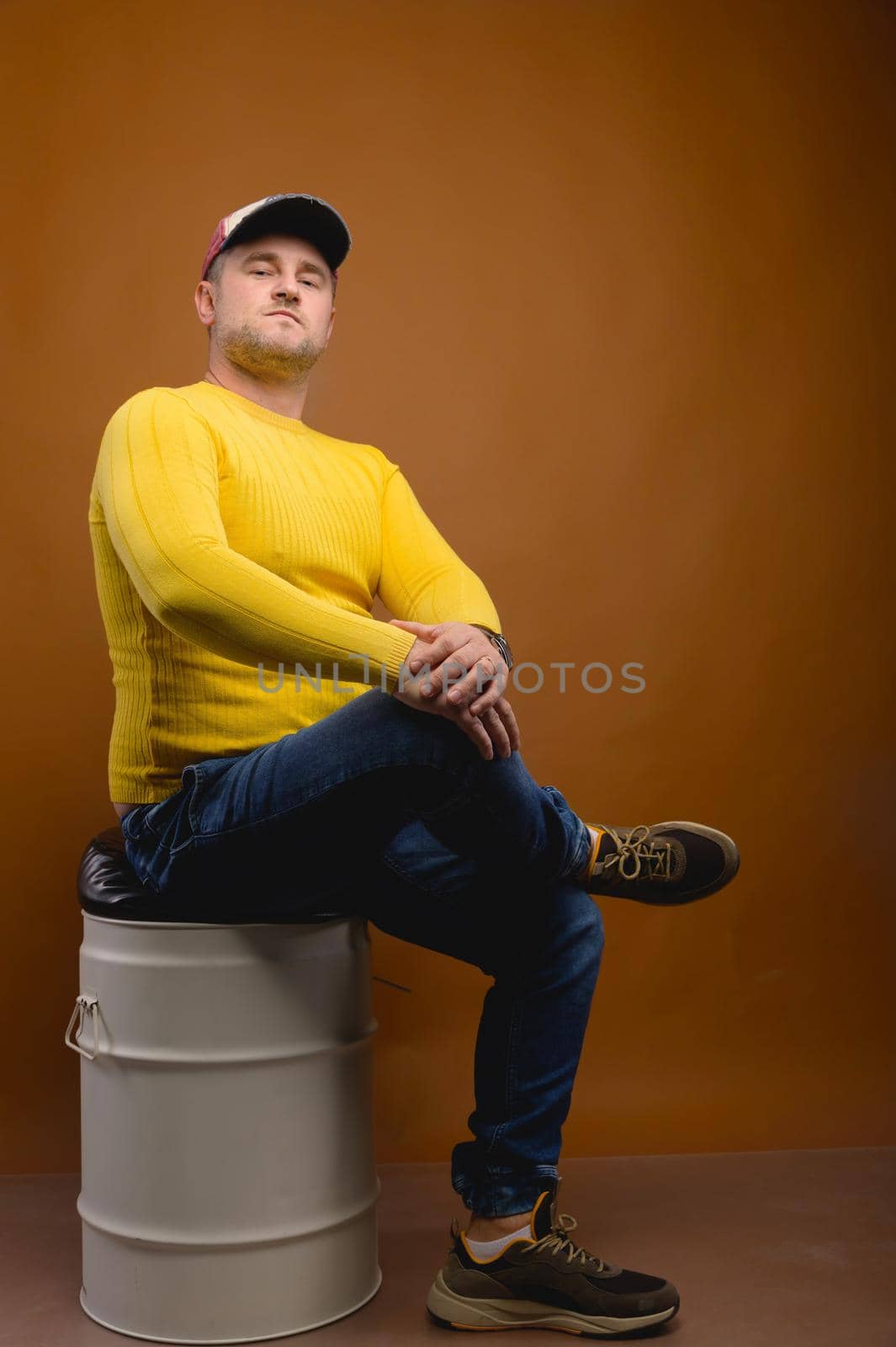 Portrait of an attractive friendly Caucasian man in a cap and yellow sweater on a brown background. Nice middle aged guy in casual clothes. Looks into the camera. Copy space.