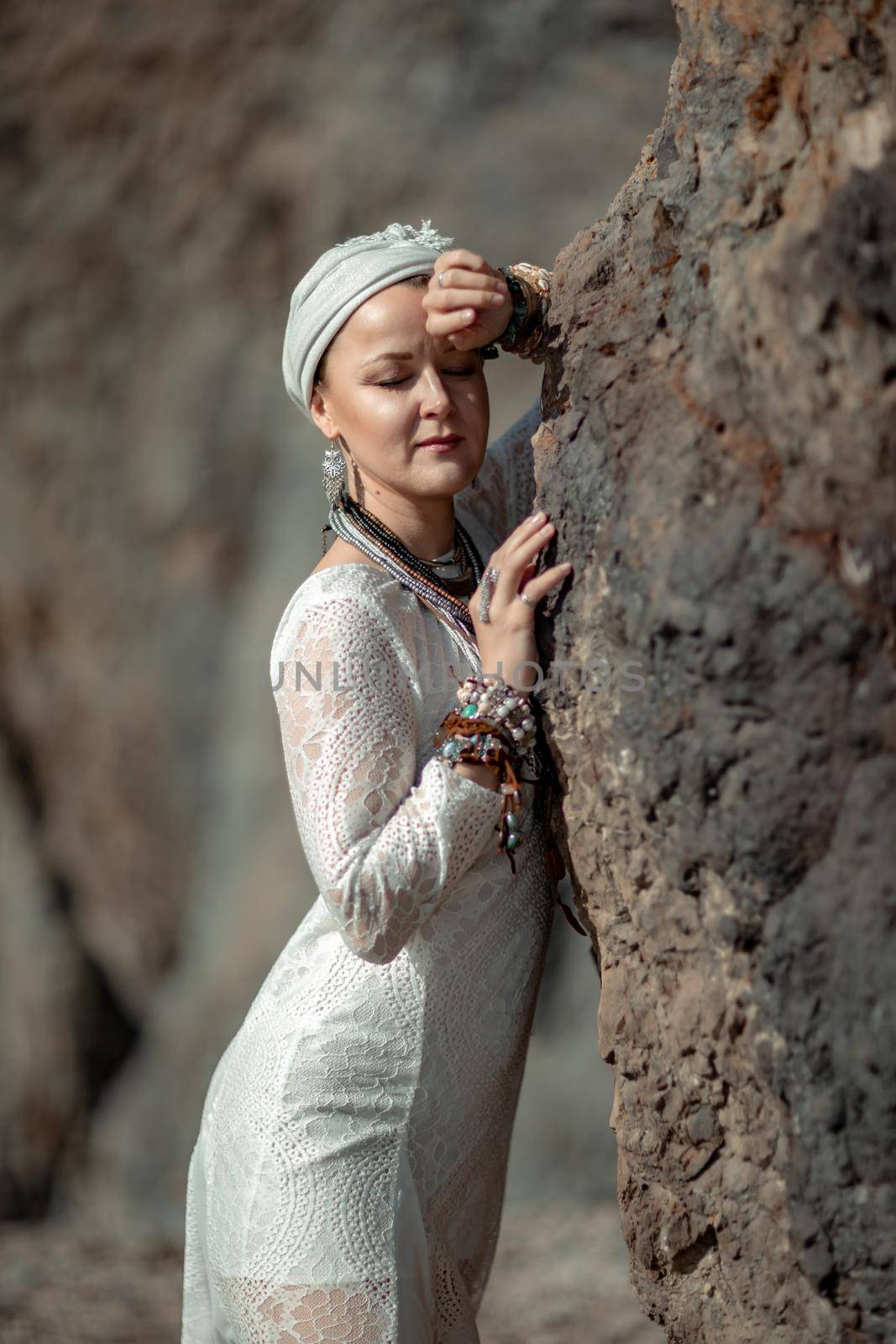 Middle aged woman looks good with blond hair, boho style in white long dress on the beach decorations on her neck and arms