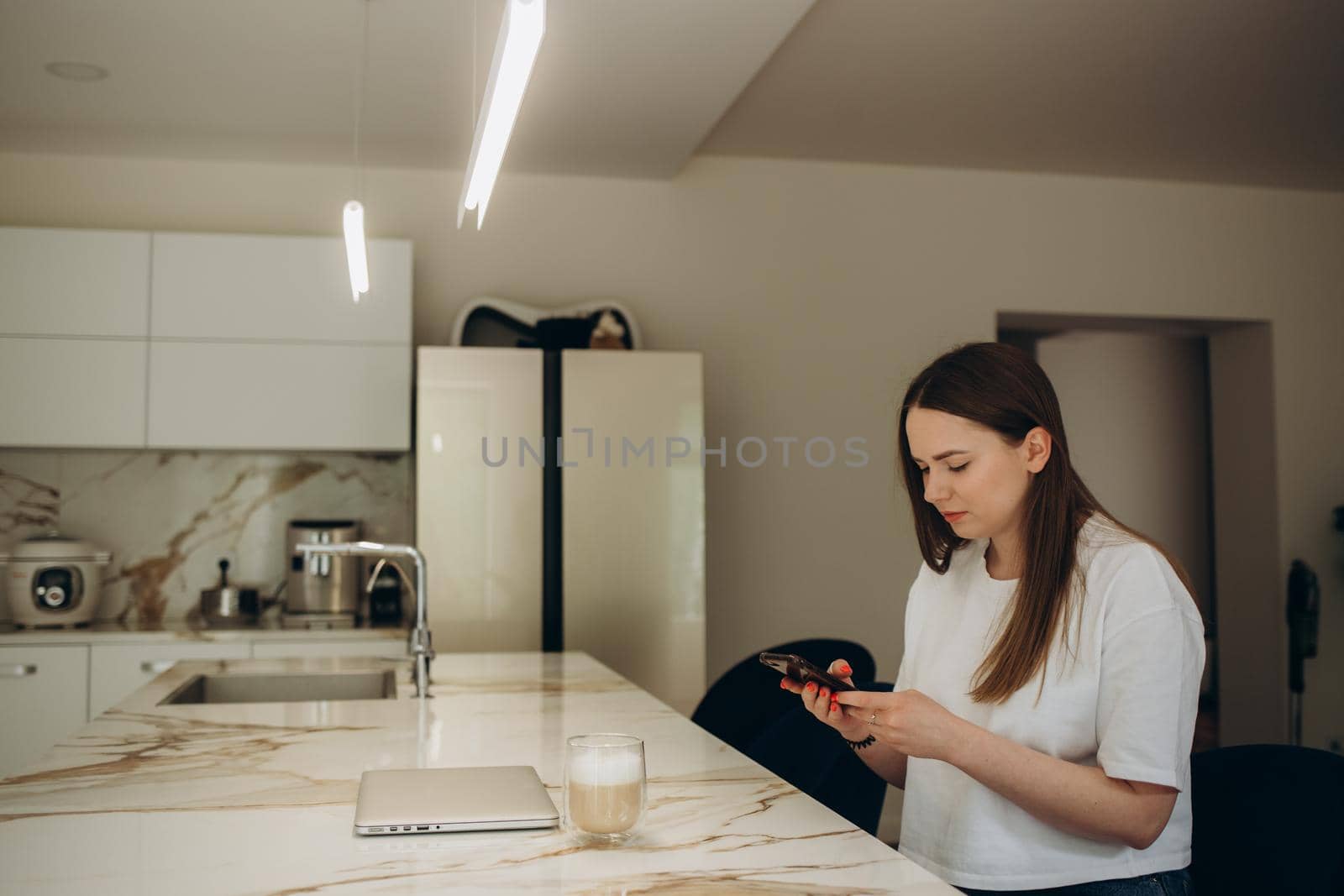 Beautiful woman drinking coffee and using the phone in the kitchen. Young woman enjoying in morning. by fentonroma