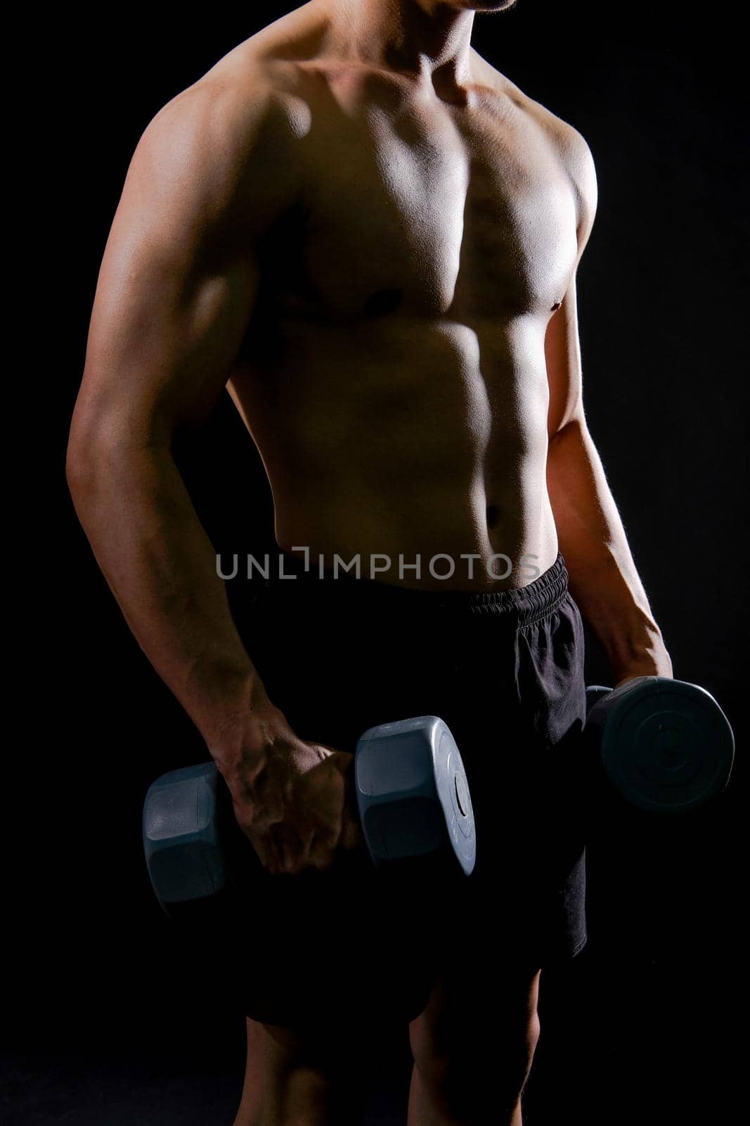 portrait of athletic muscular bodybuilder man with naked torso six pack abs working out with dumbbell. fitness sport exercise concept