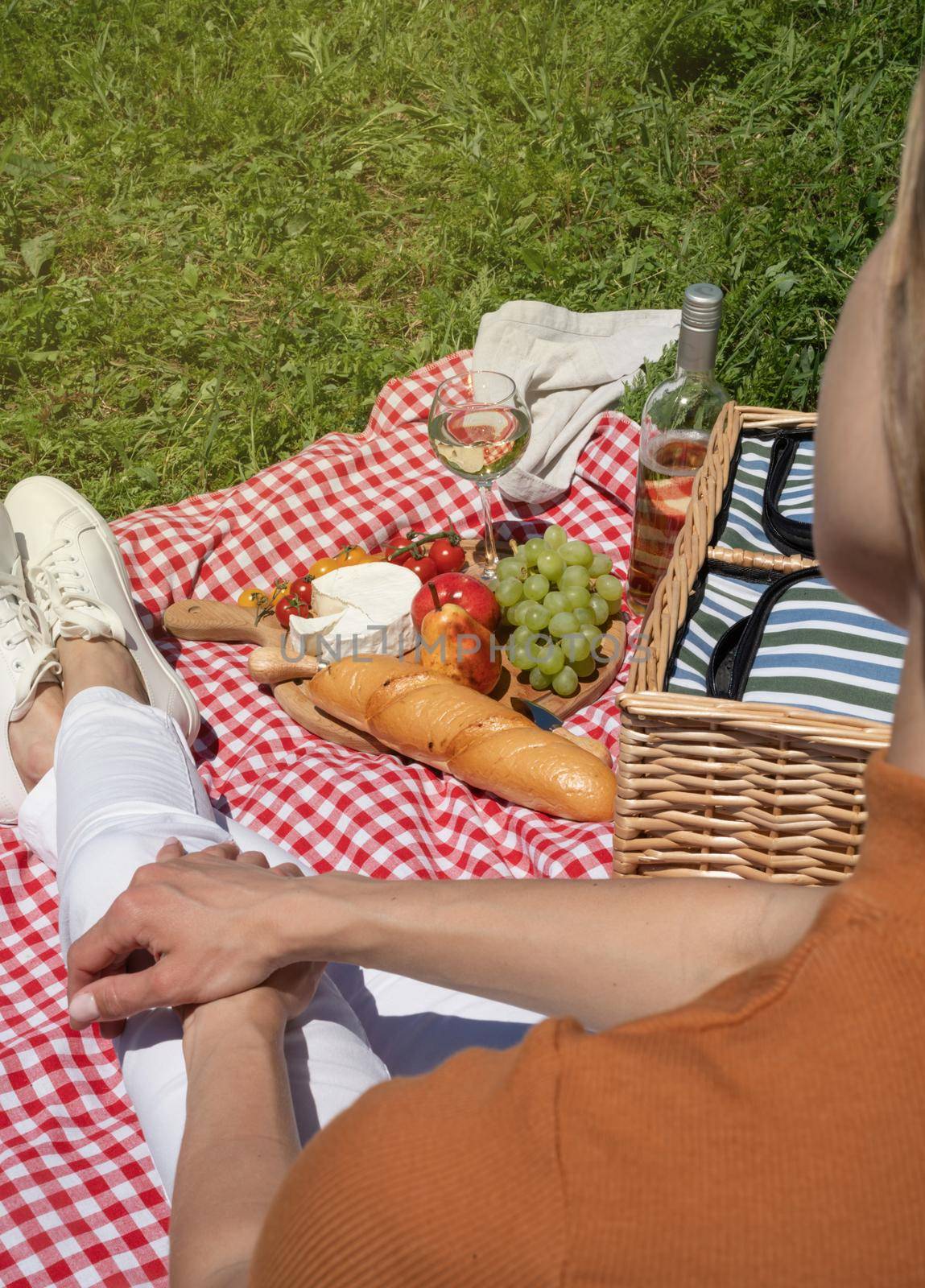 unrecognizable young woman in white pants outside having picnic, eating and playing guitar. Summer fun and leisure