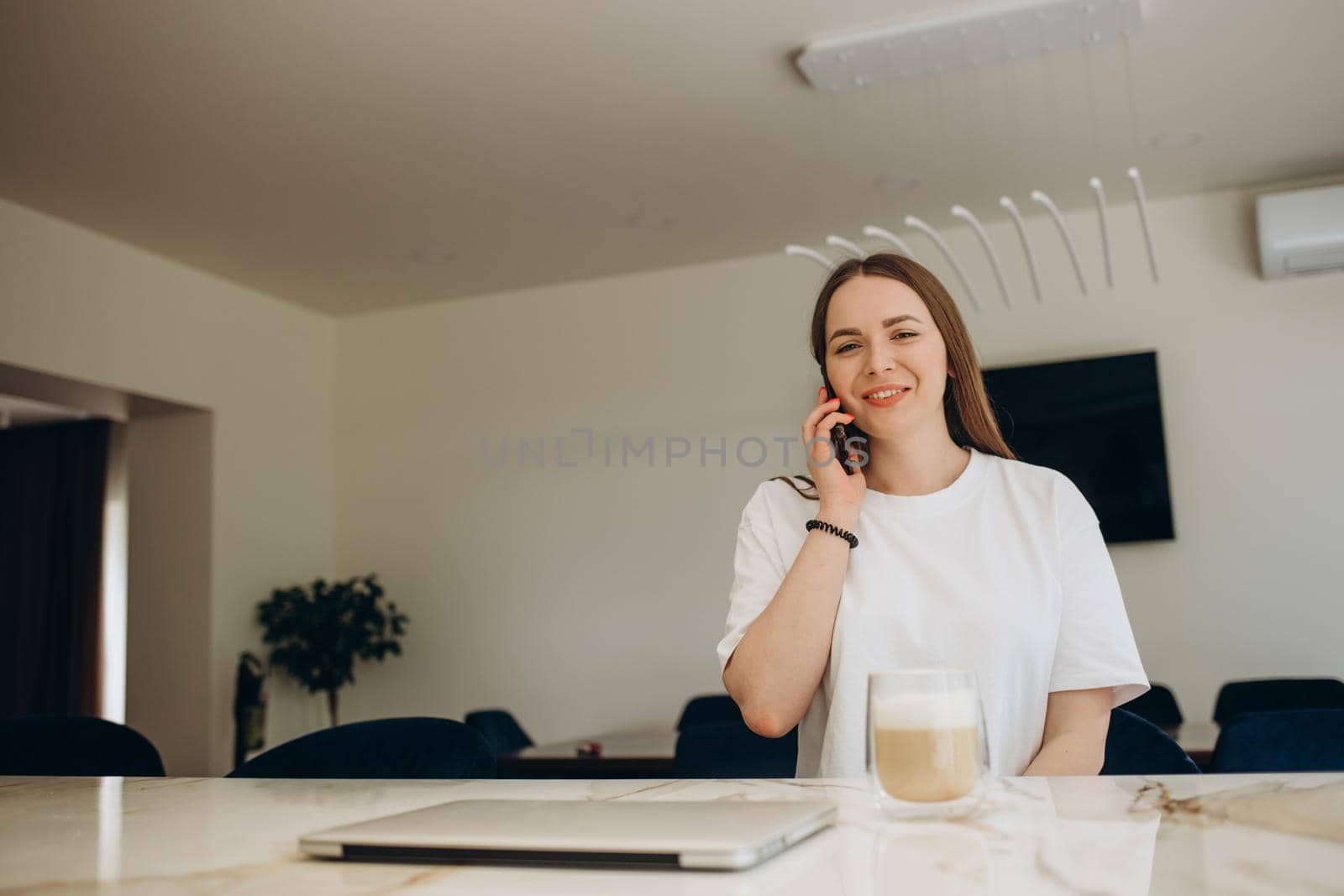 Young attractive smiling Latina woman talking on phone while cooking alone in kitchen. Housewife holds cellphone chatting distracted from healthy vegetarian food preparation. Chores, lifestyle concept by fentonroma
