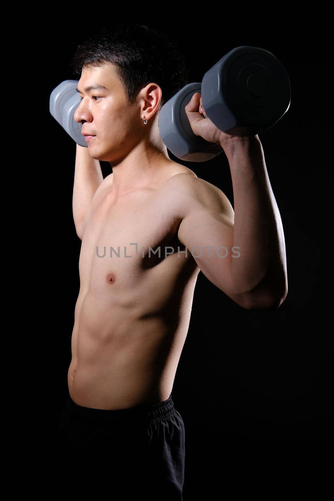 portrait of athletic muscular bodybuilder man with naked torso six pack abs working out with dumbbell. fitness sport exercise concept