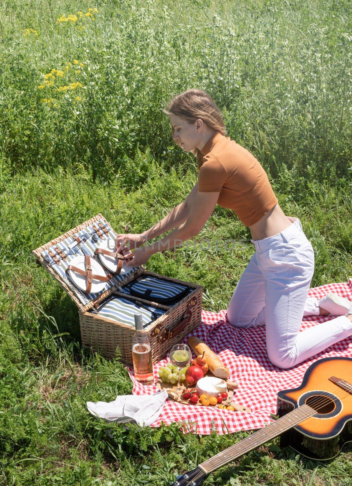 Young woman in summer clothes unpacking picnic basket outdoors, ready to have a picnic