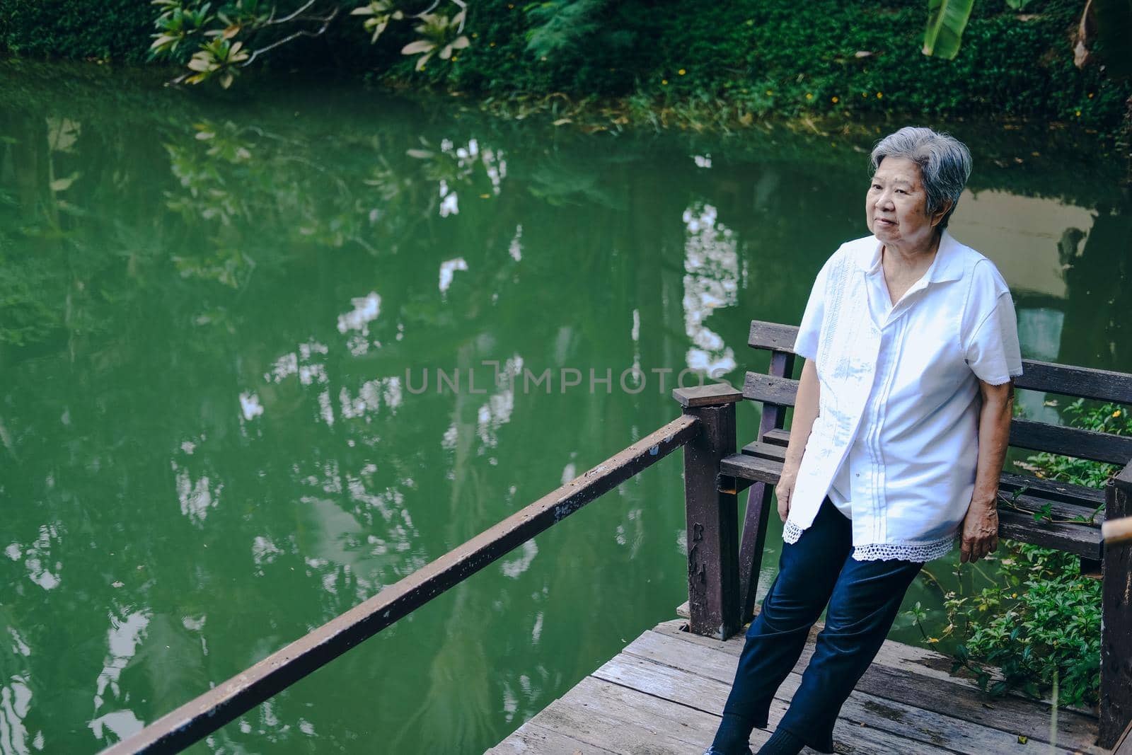 old elder woman resting near pond. asian elderly female relaxing outdoors. senior leisure lifestyle