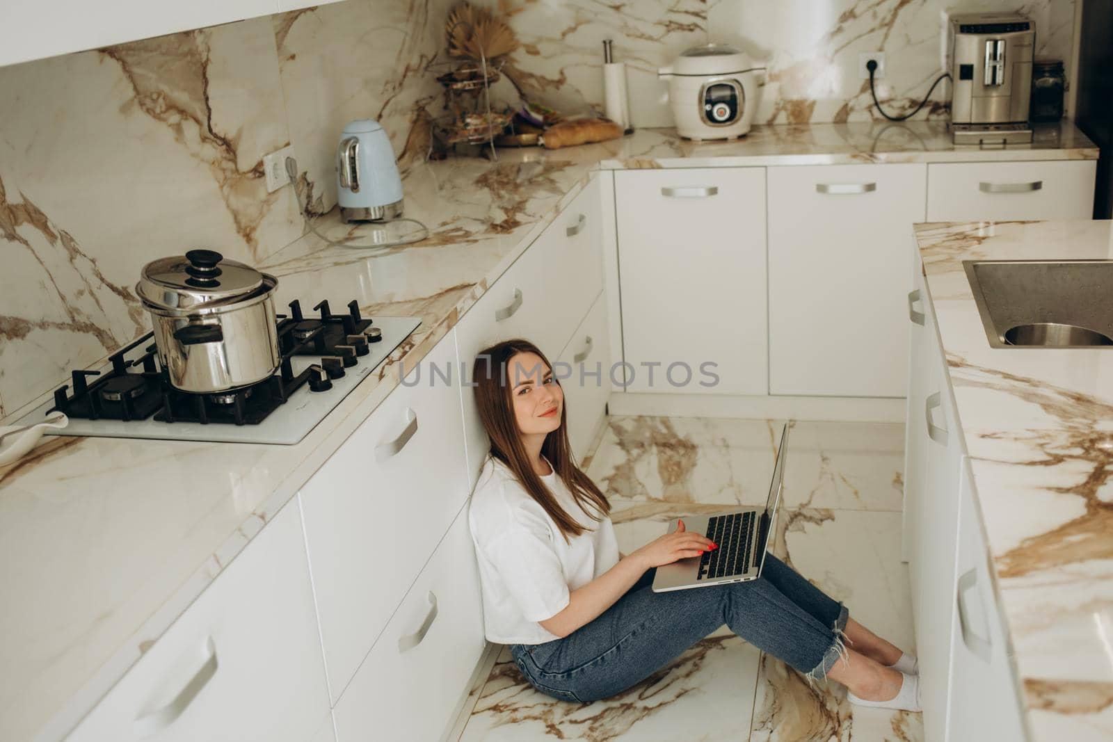 Beautiful woman working with laptop sitting on the floor in the kitchen.