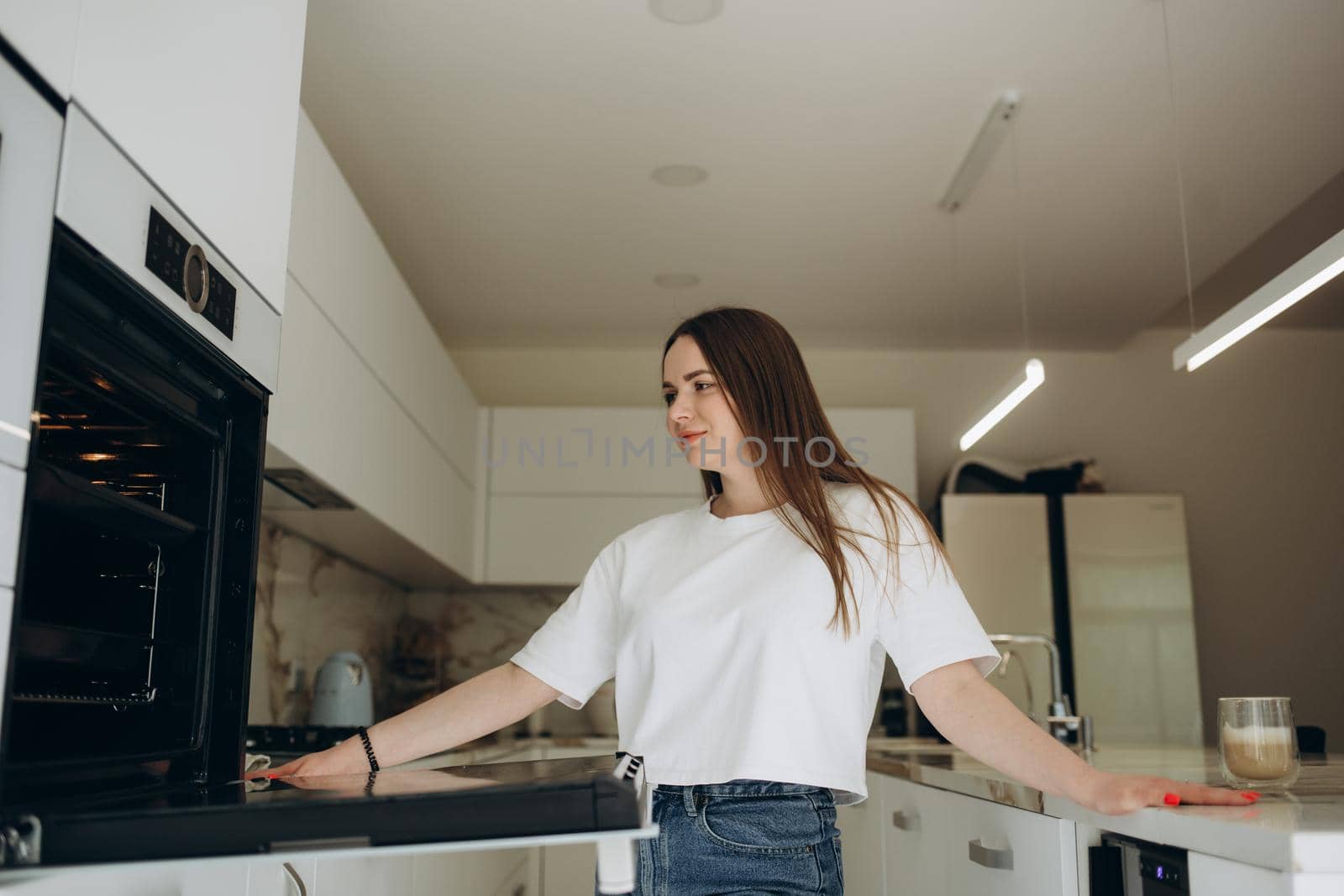 Portrait of happy girl putting baking tray in kitchen oven.