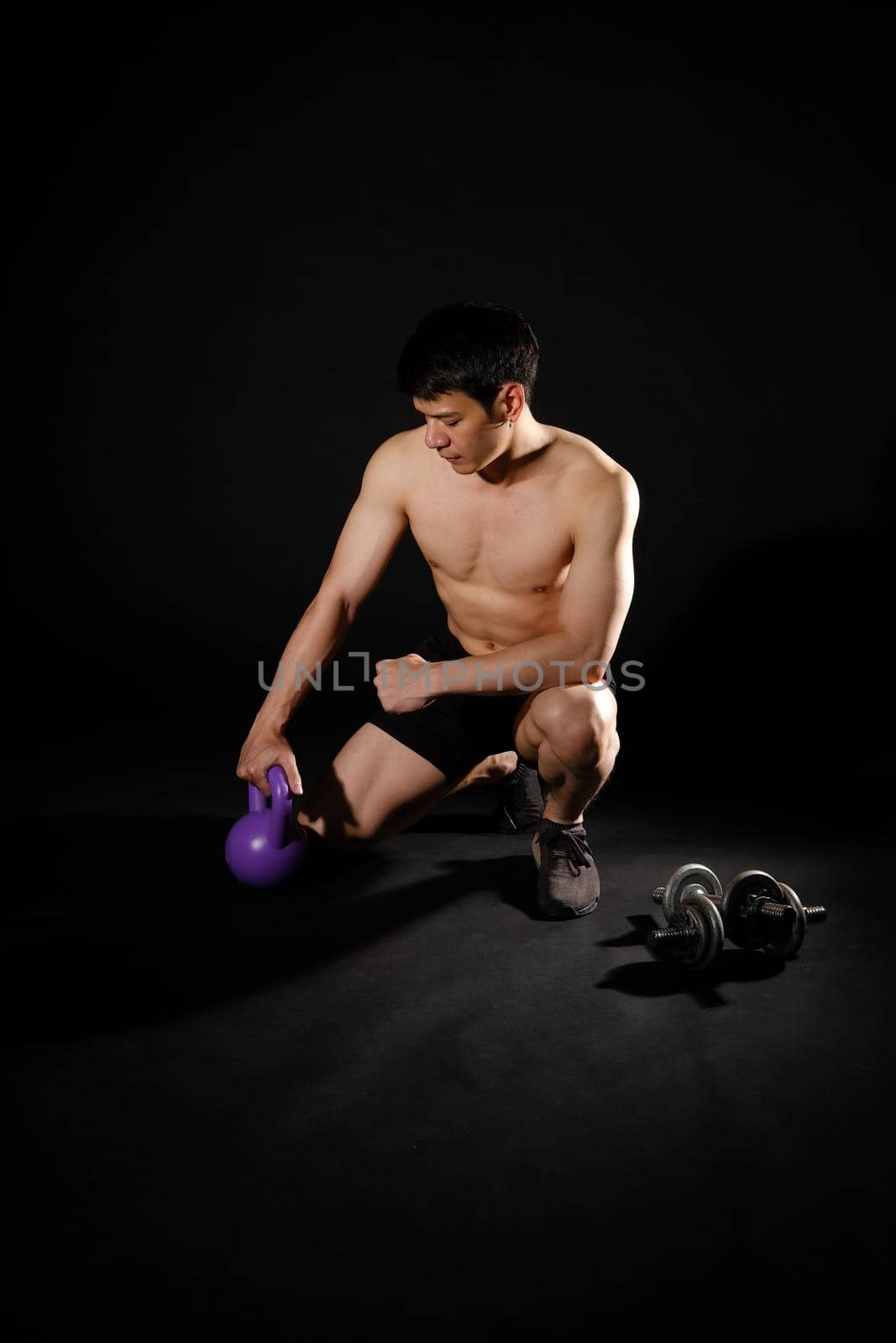 portrait of athletic muscular bodybuilder man with naked torso six pack abs working out with kettle bell. fitness sport exercise concept