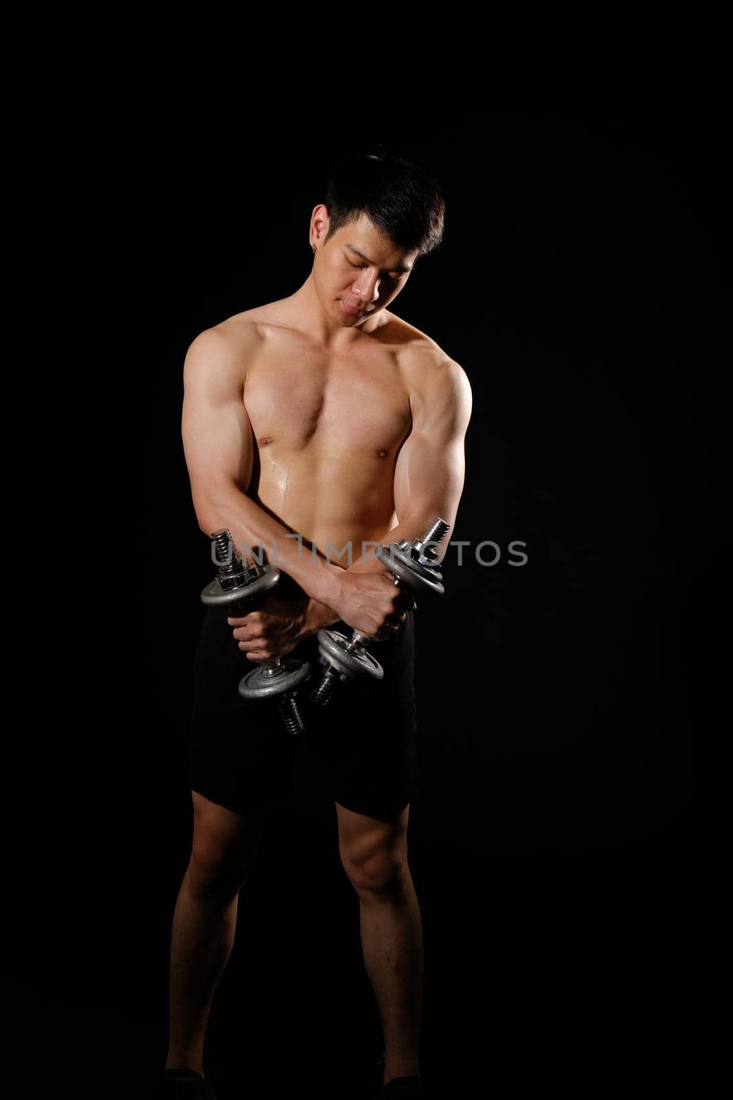 portrait of athletic muscular bodybuilder man with naked torso six pack abs working out with dumbbell. fitness sport exercise concept