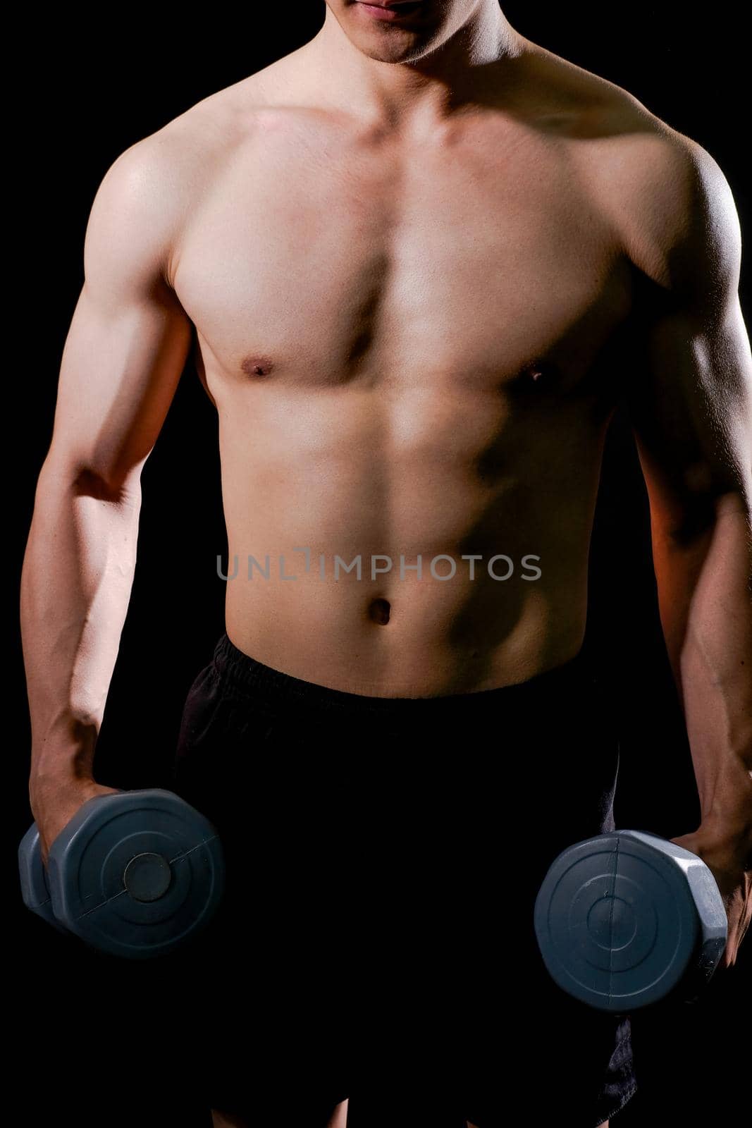 portrait of athletic muscular bodybuilder man with naked torso six pack abs working out with dumbbell. fitness sport exercise concept