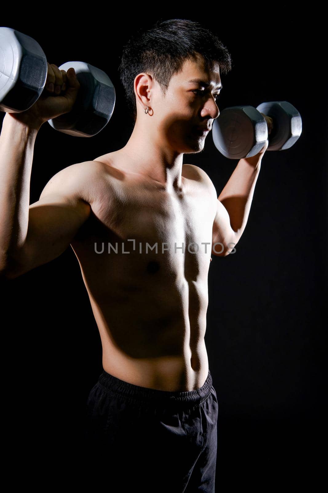 portrait of athletic muscular bodybuilder man with naked torso six pack abs working out with dumbbell. fitness sport exercise concept