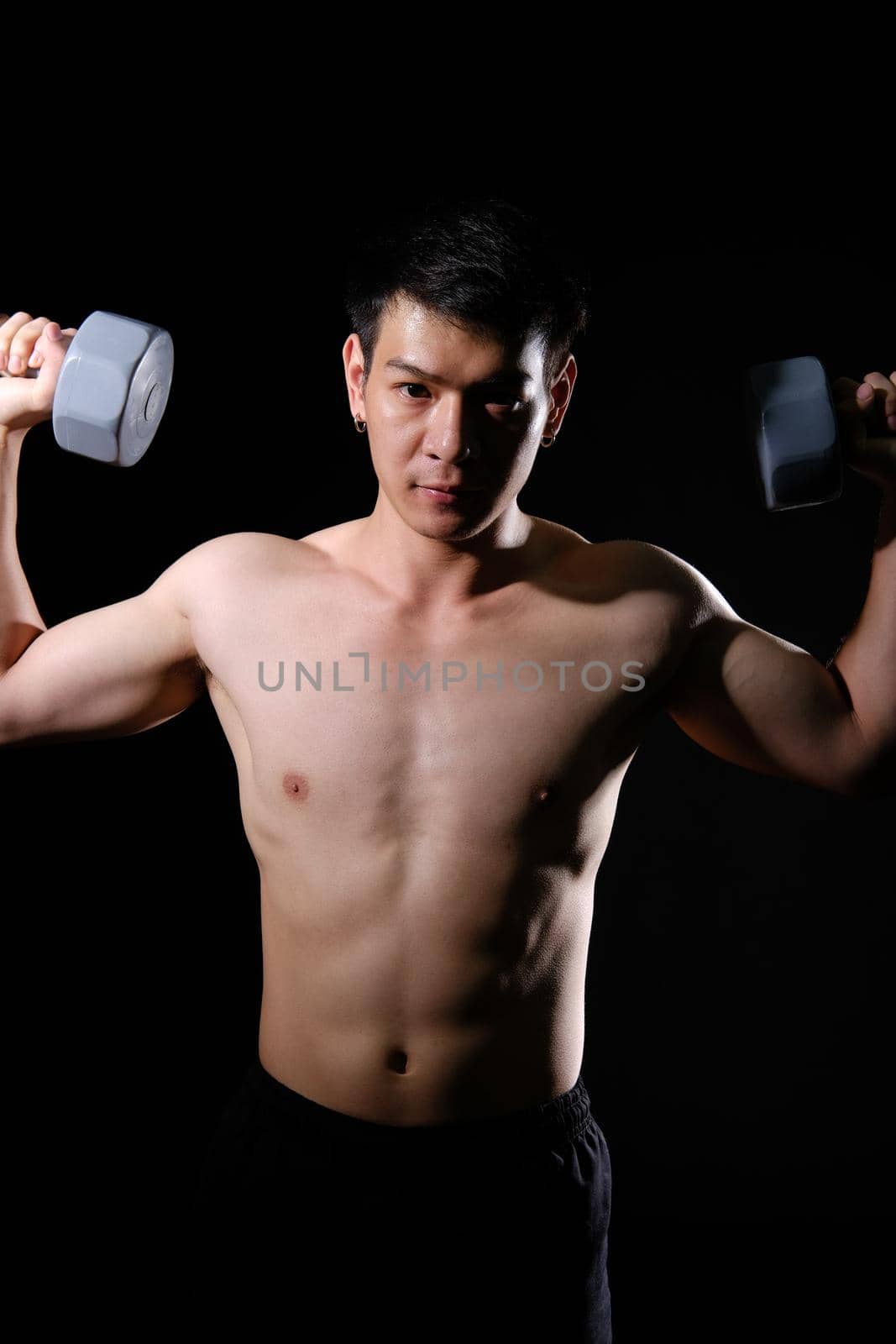 portrait of athletic muscular bodybuilder man with naked torso six pack abs working out with dumbbell. fitness sport exercise concept