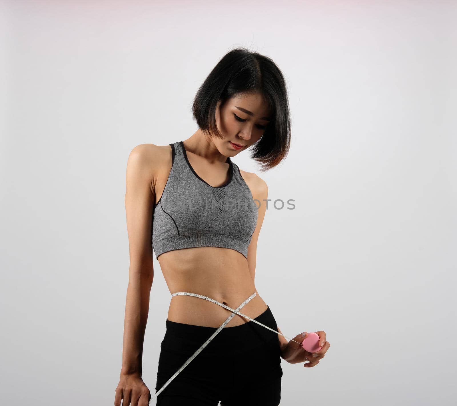 sporty fitness woman in sportswear with measuring waist with tape on white background. healthy sport lifestyle