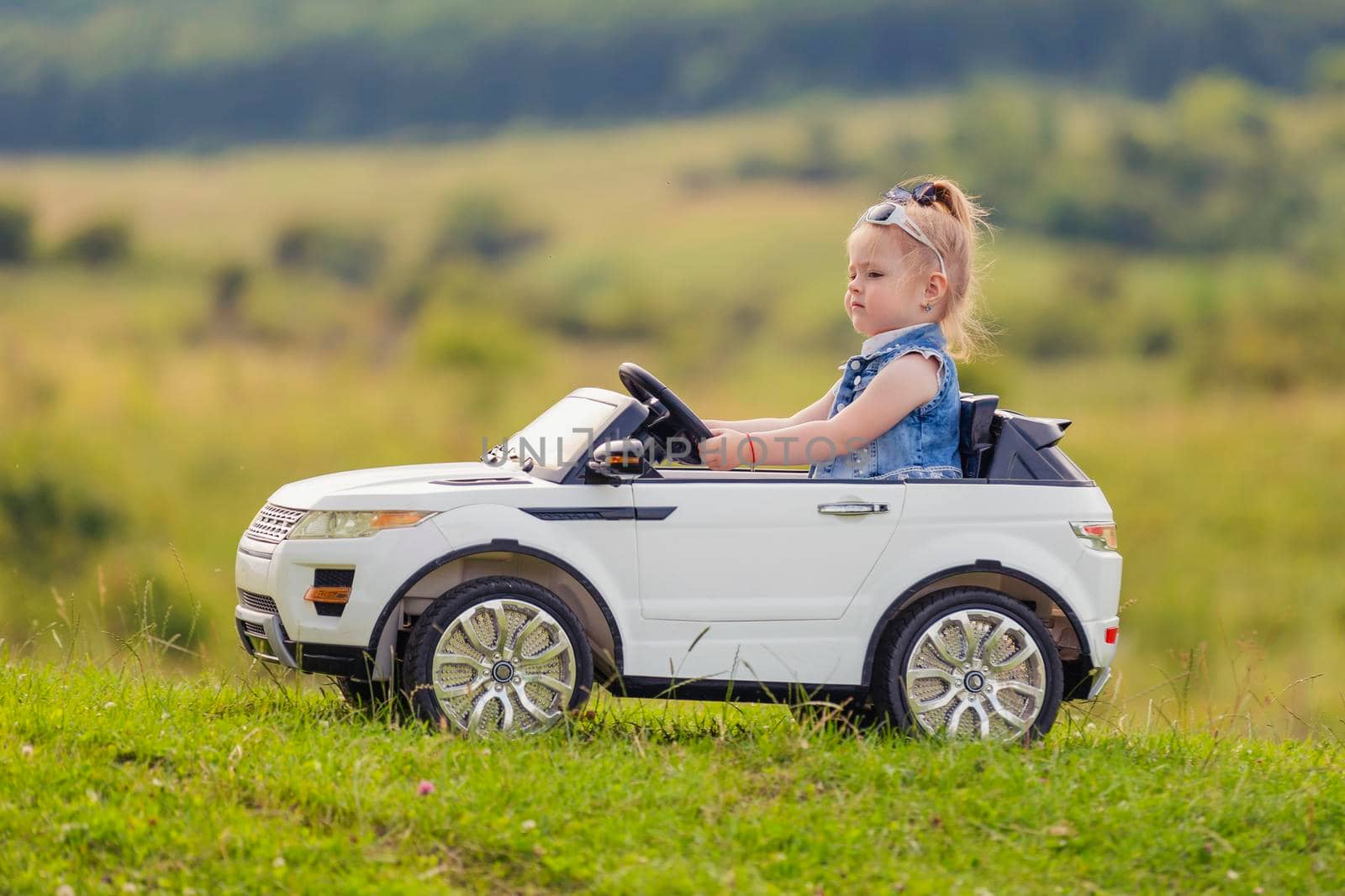 little girl rides on a children's car on a green lawn