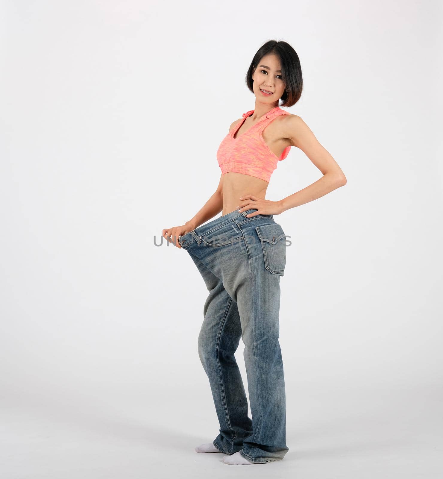 sporty fitness woman in loose jeans after losing weight on white background. healthy sport by pp99