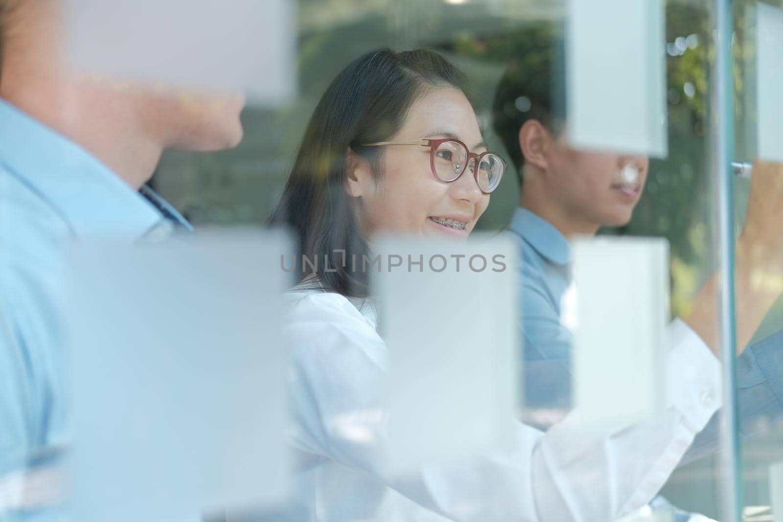 business people working planning discussing idea with sticky reminder note on glass wall at workplace