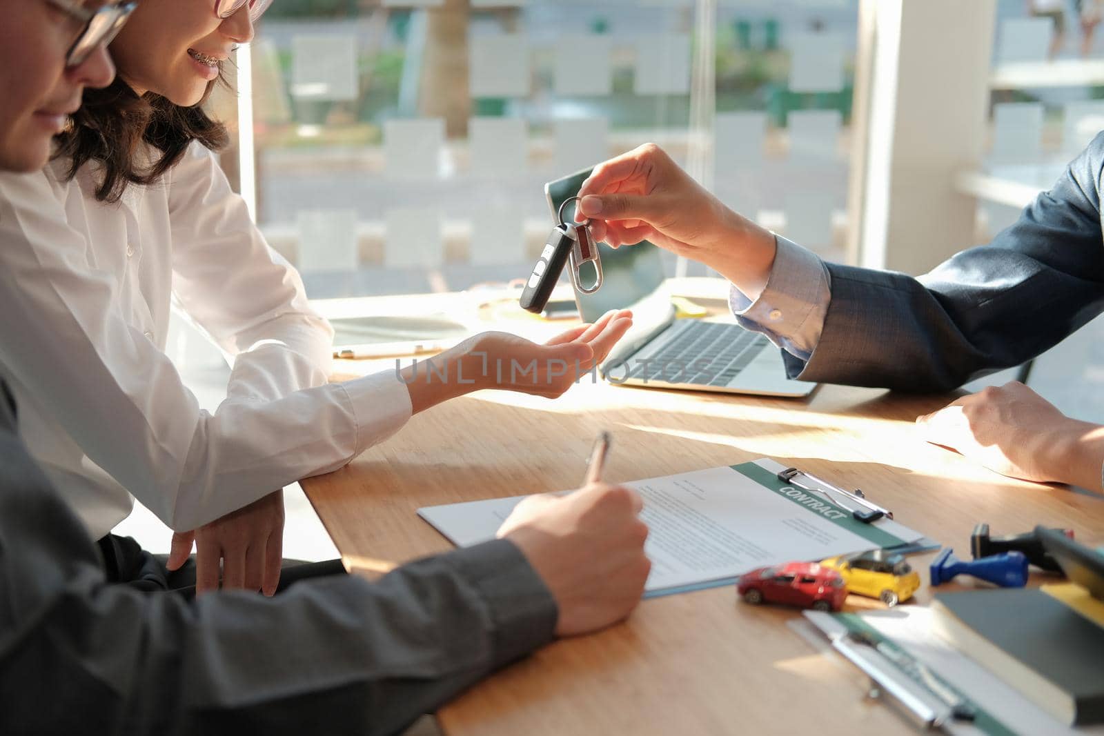 dealer salesman giving car key to new owner. client signing insurance document or rental car lease form