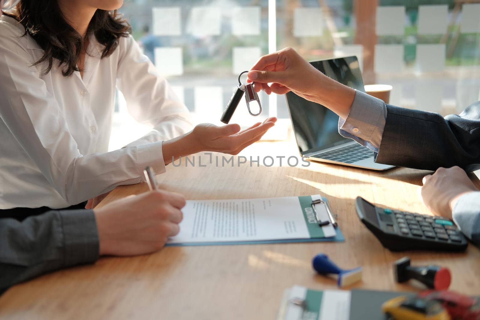 dealer salesman giving car key to new owner. client signing insurance document or rental car lease form