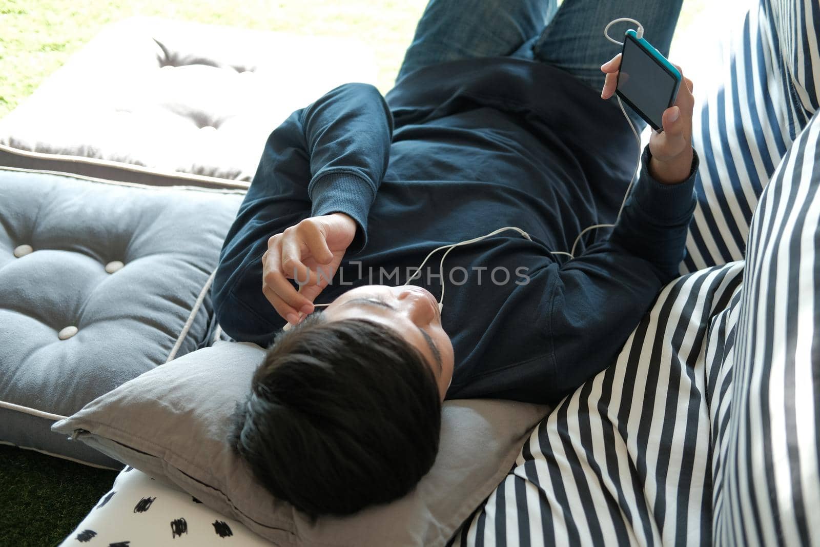 asian male teenager man listening to music from smart mobile phone while lying on floor at home