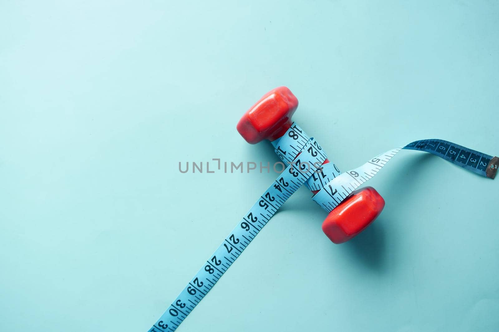 Fitness concept with dumbbell and measurement tape on table .