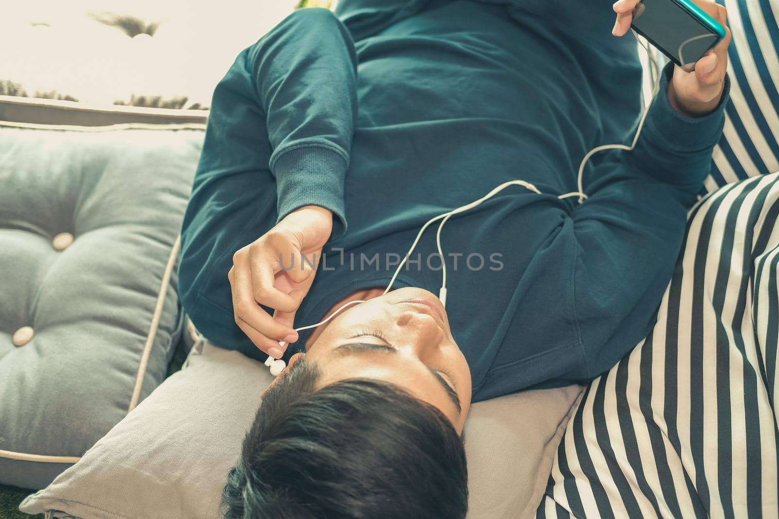 asian male teenager man listening to music from smart mobile phone while lying on floor at home