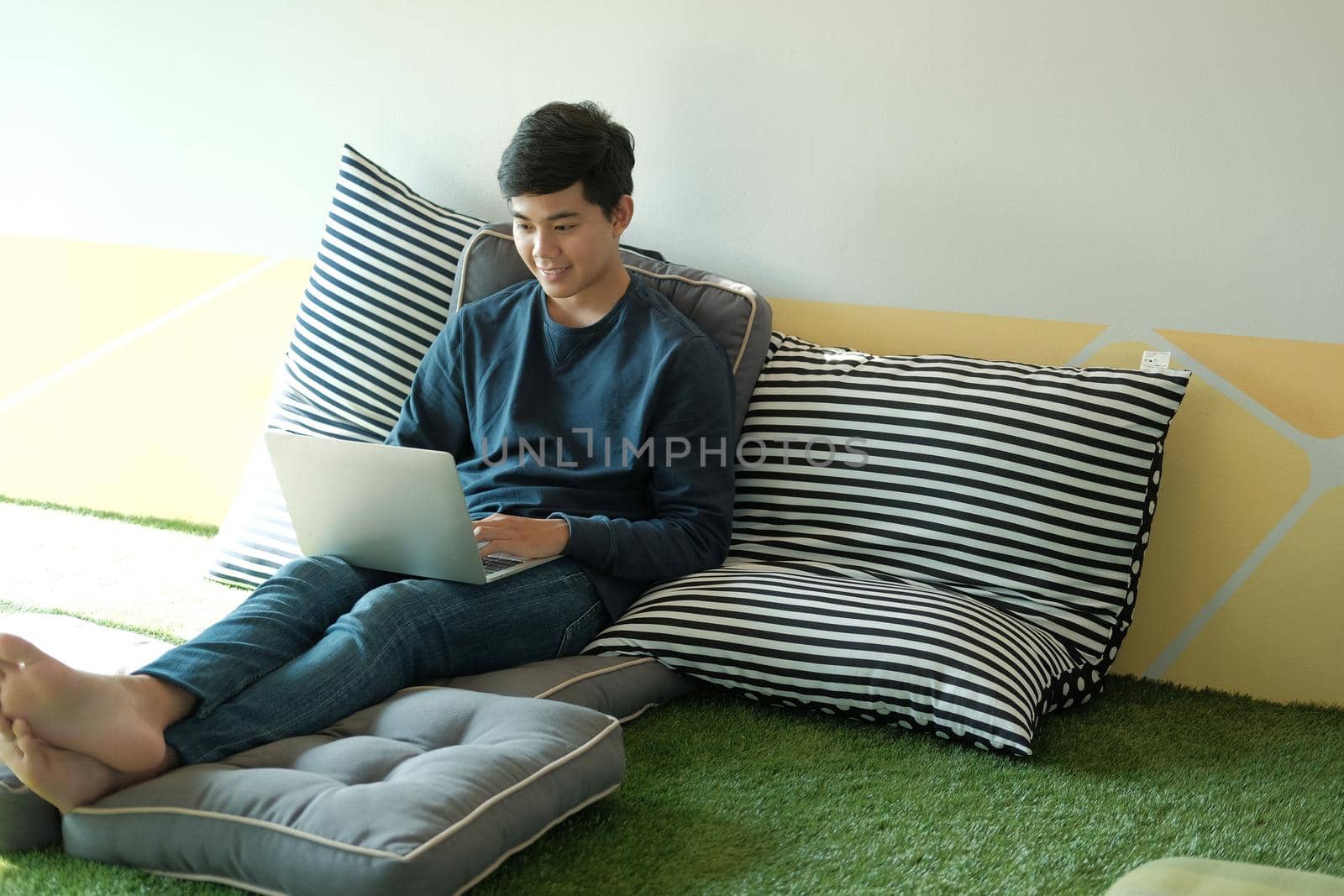 man sitting on floor in living room using computer at home. male teenager student studying doing assignment