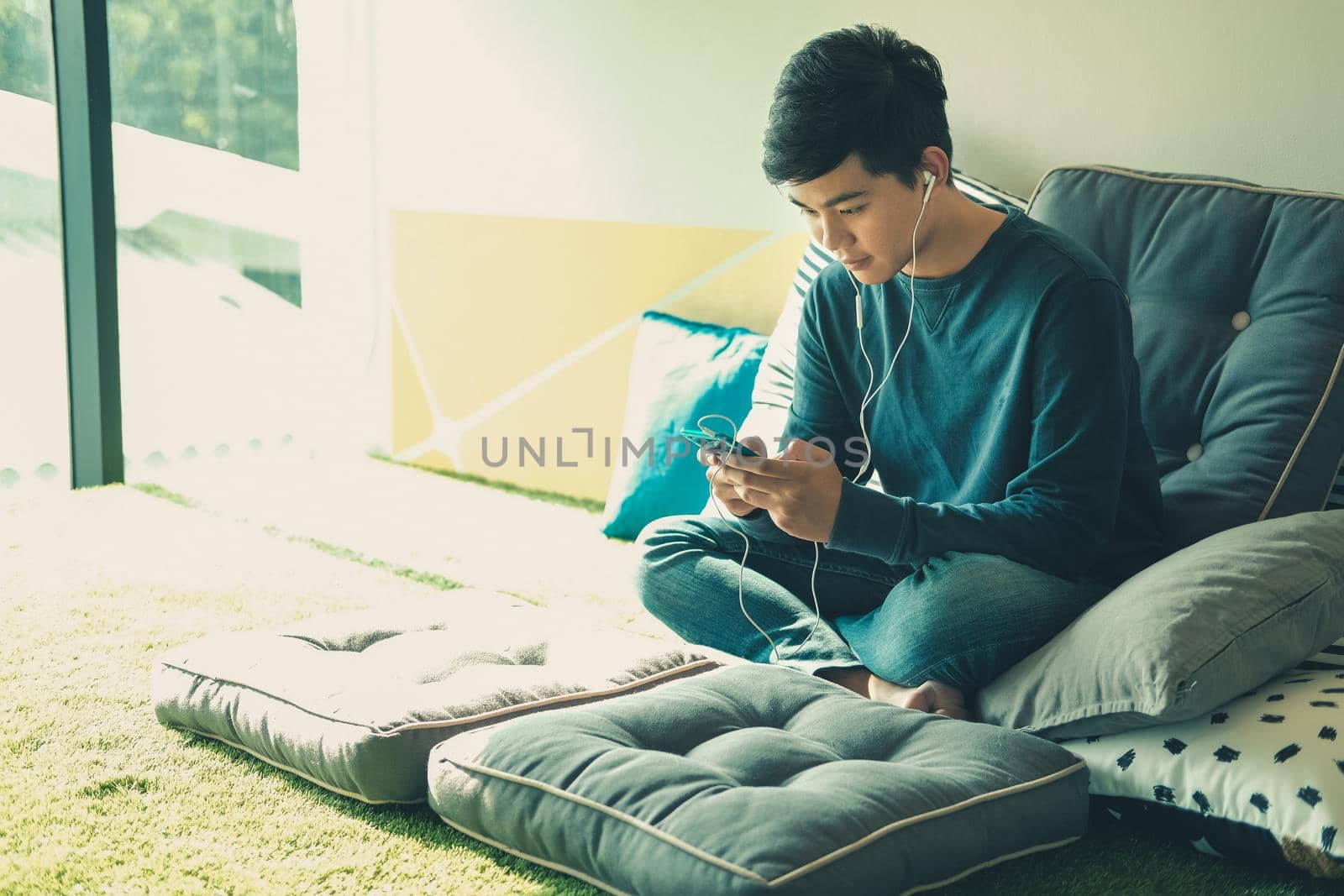 asian male teenager man listening to music from smart mobile phone while sitting on floor at home