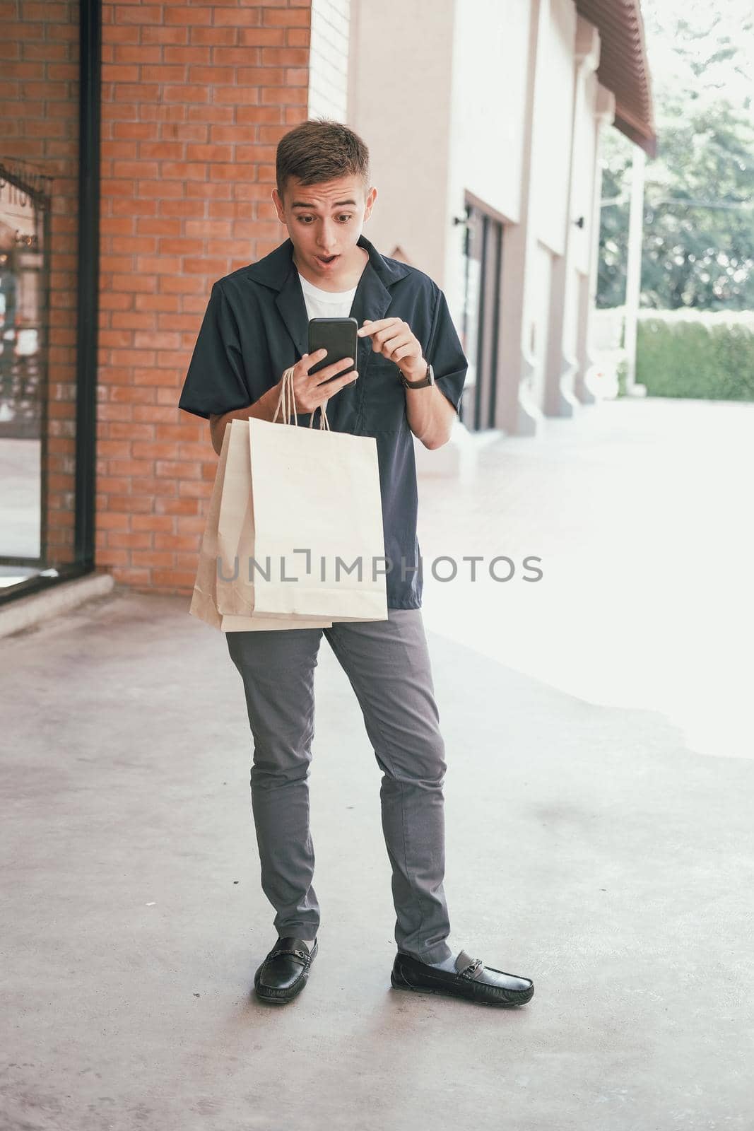 surprised man holding paper shopping bags & mobile smart phone.  by pp99