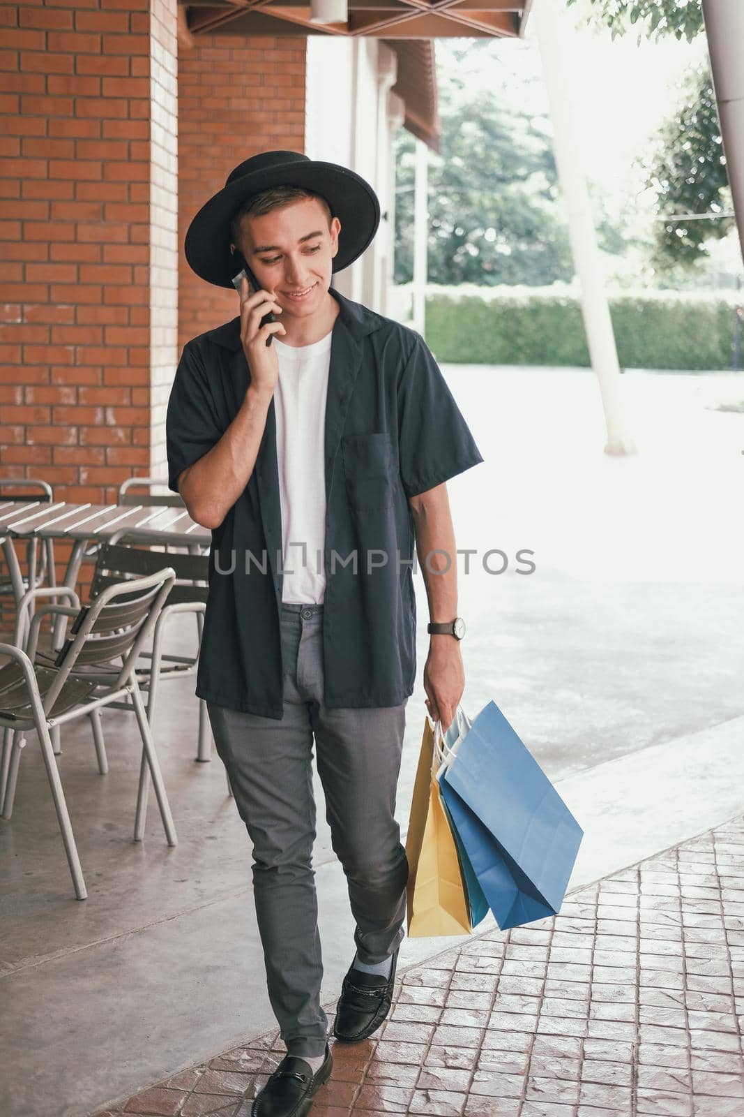 man holding paper shopping bags & talking on mobile smart phone. consumerism lifestyle