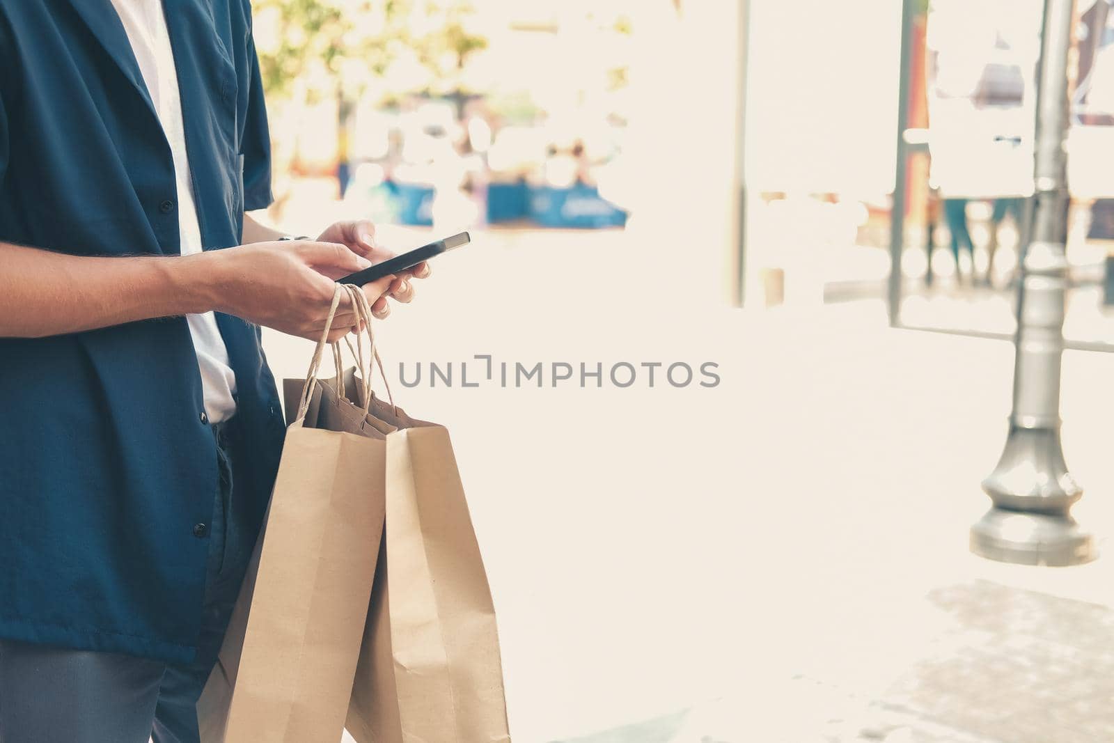 man holding paper shopping bags & using mobile smart phone. consumerism lifestyle