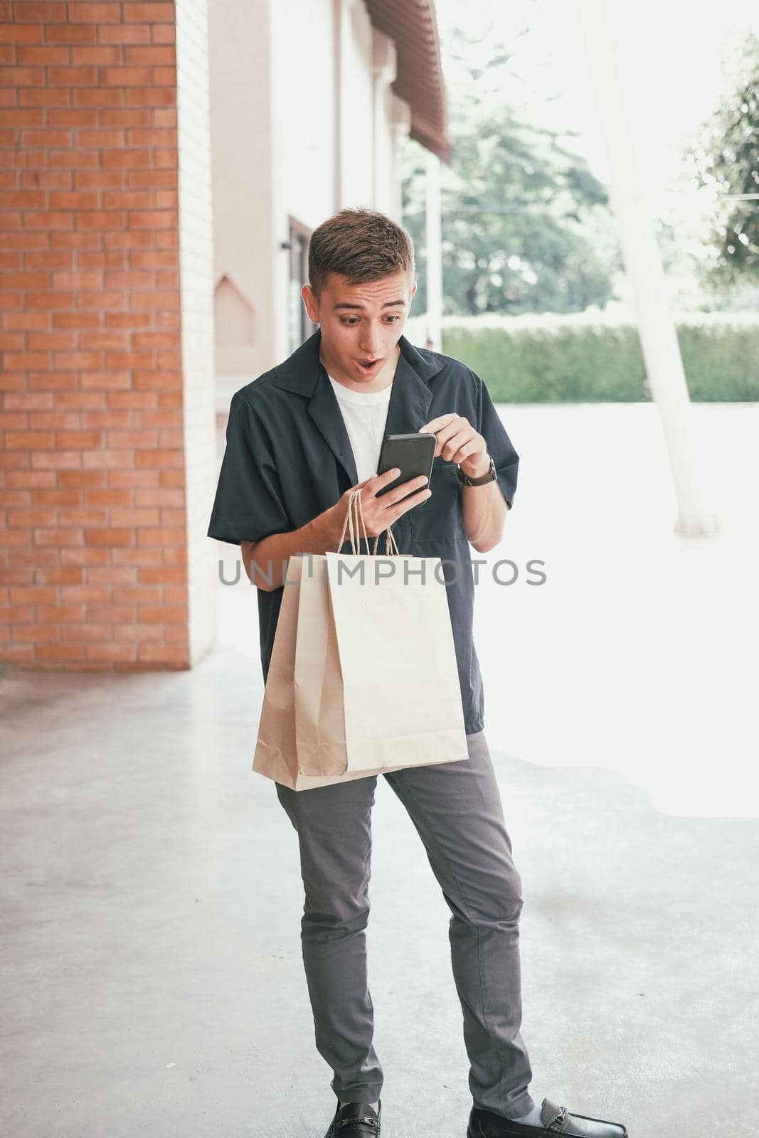 surprised man holding paper shopping bags & mobile smart phone. by pp99