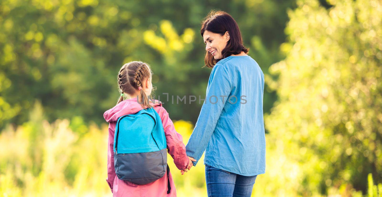 Mother meeting primary schoolgirl after classes on car parking outdoors during virus epidemic