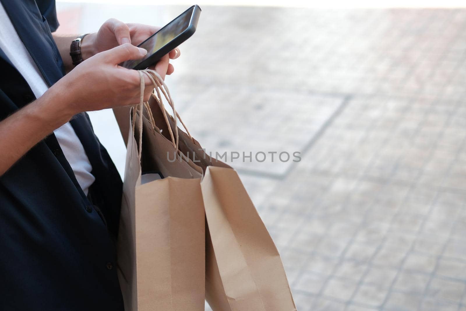 man holding paper shopping bags & using mobile smart phone. consumerism lifestyle