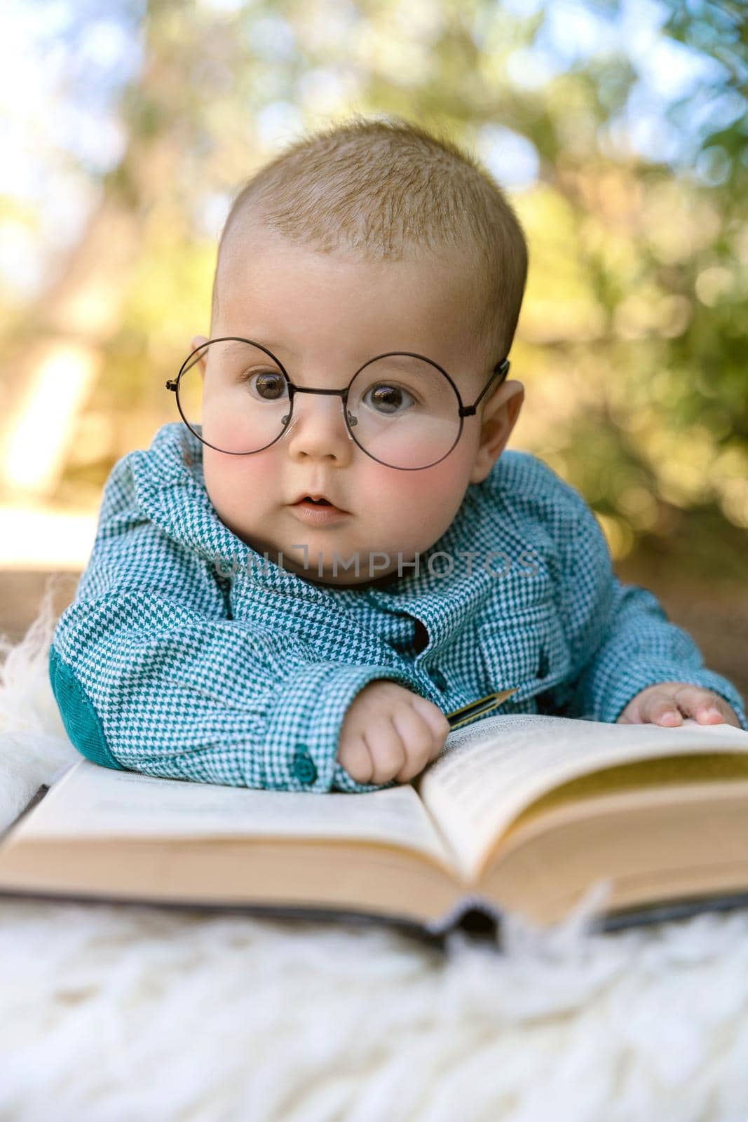 Funny portrait of cute baby in glasses. The baby lies on his stomach and reads an old book on a green background. High quality photo