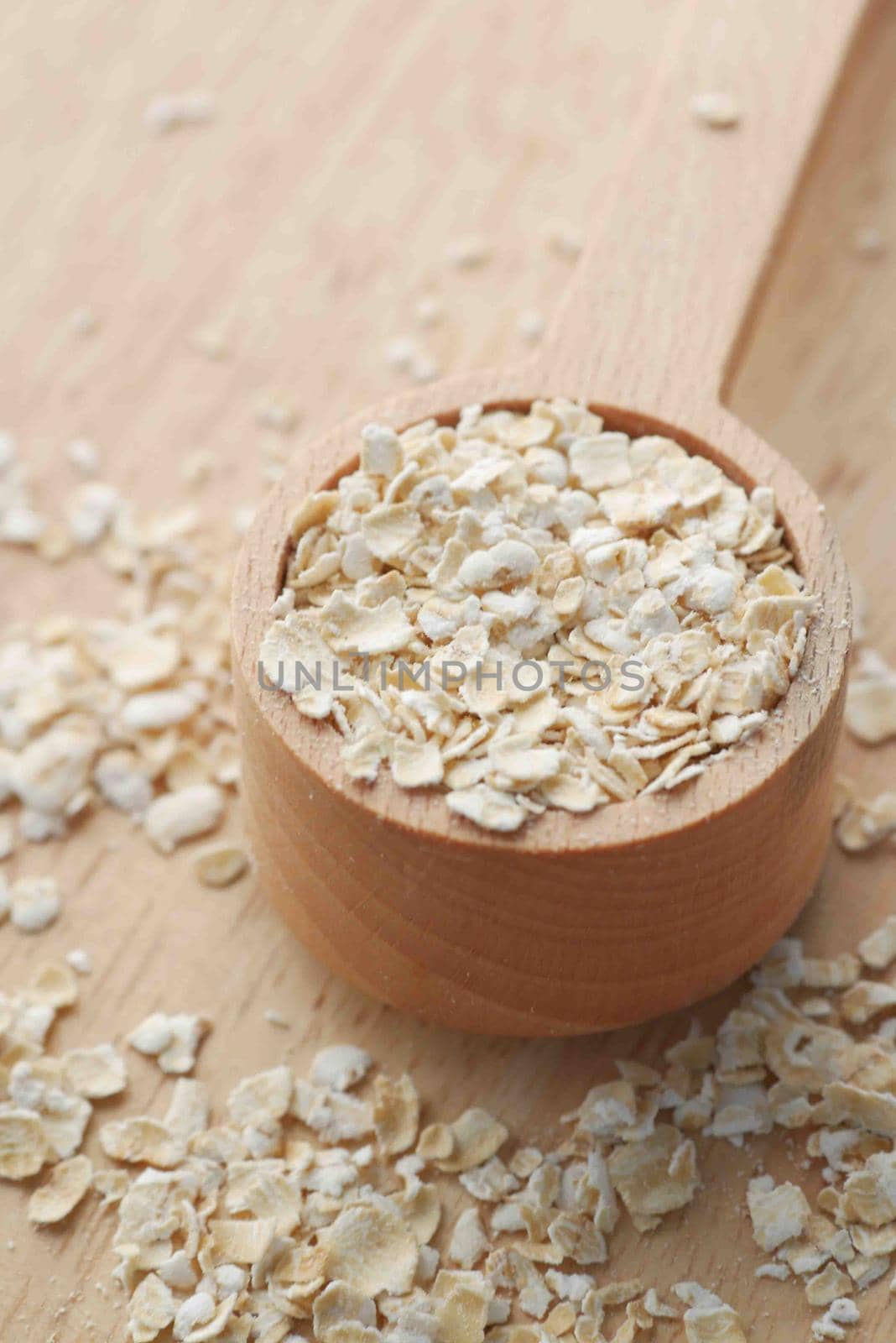 Close up of oats flakes on spoon on table .