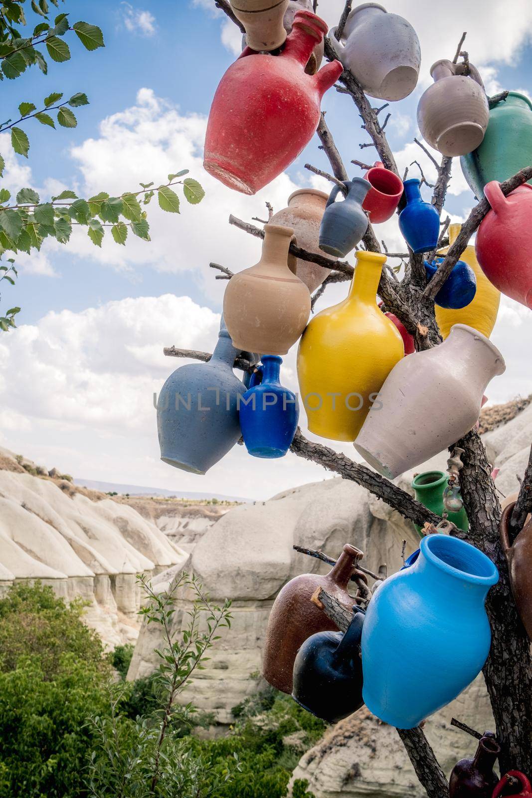 Colorful ceramic vases hanging on tree branch on sand mountain background in Turkey