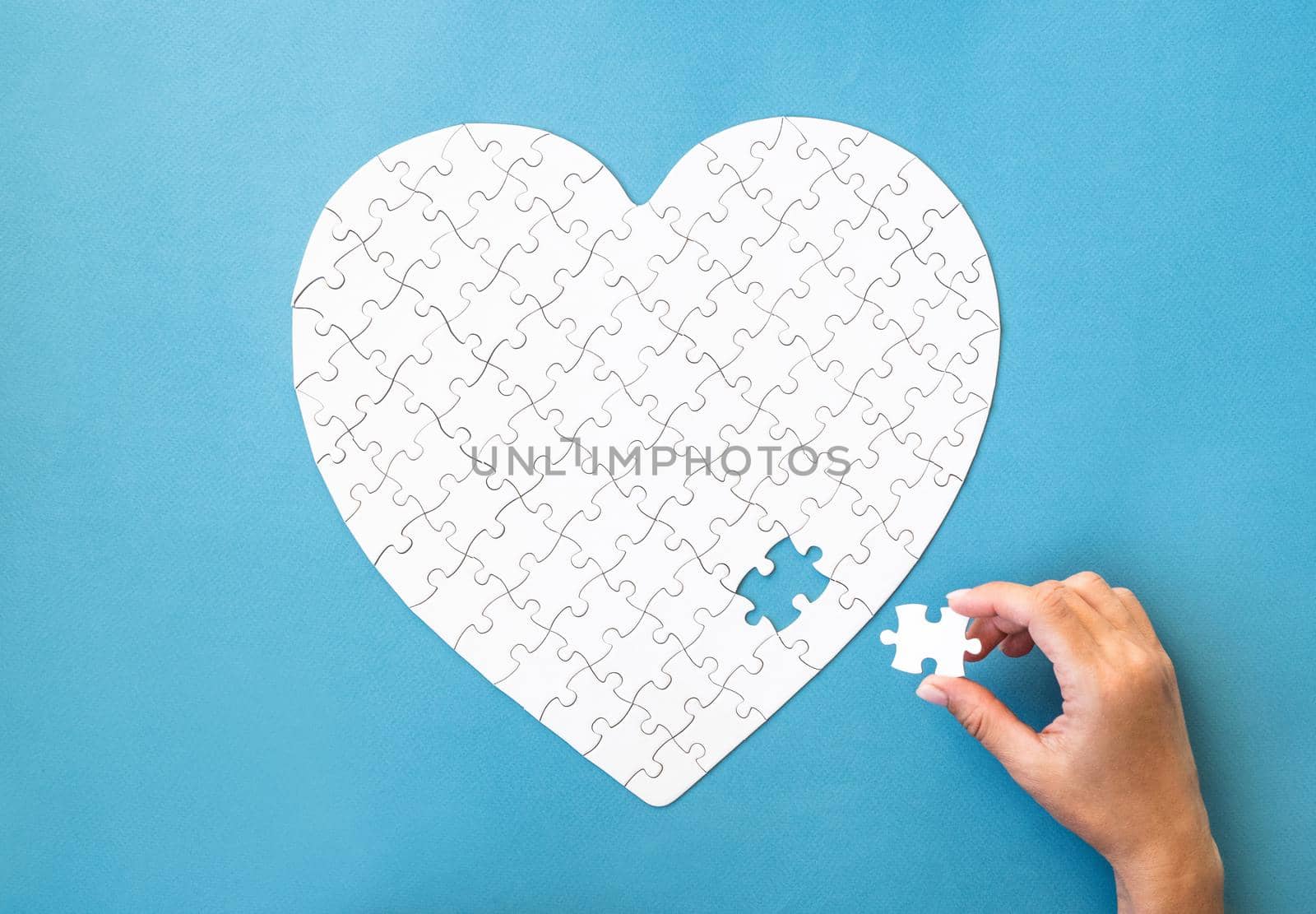 White puzzle in heart shape. Hand with white details of puzzle on blue background.