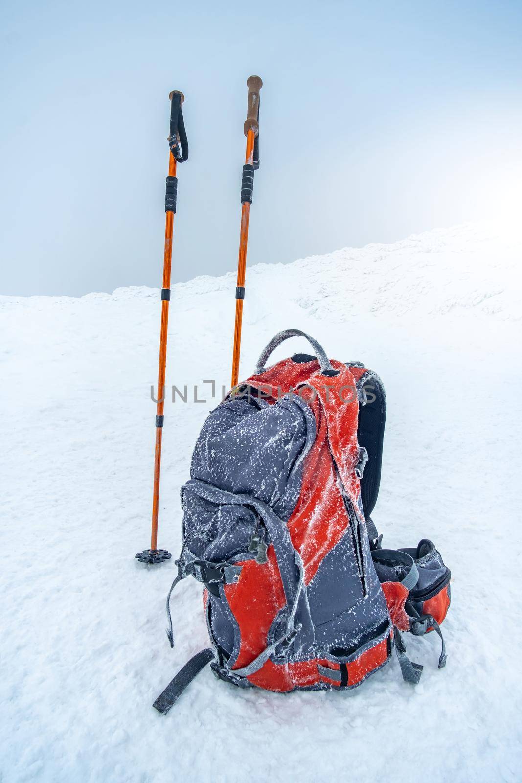 Trekking sticks and backpack standing on snow under clear winter sky