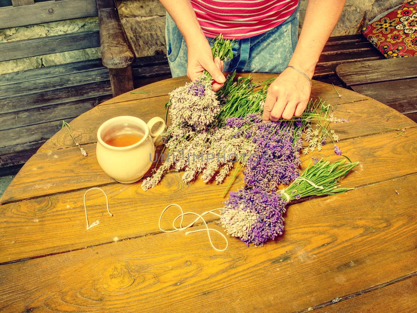 Aroma designer  workplace. Girl prepar harvested lavander stalks for drying. Rustic wooden tble with cup of herbal tea