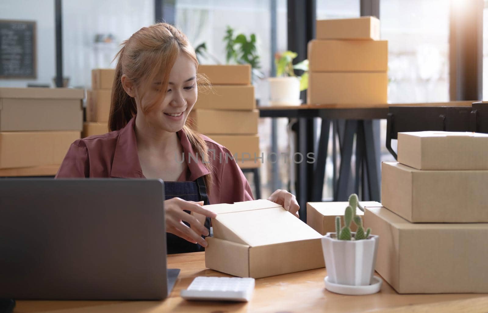 Happy young asian woman startup small business freelance holding parcel box and computer laptop and sitting on chair, Online marketing packing box delivery concept by wichayada