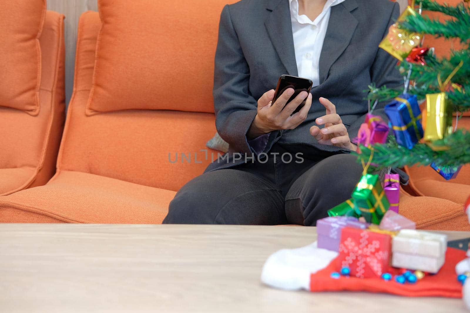man sitting on sofa using smartphone. businesswoman texting message on mobile phone during xmas. christmas holiday new year celebration season greetings