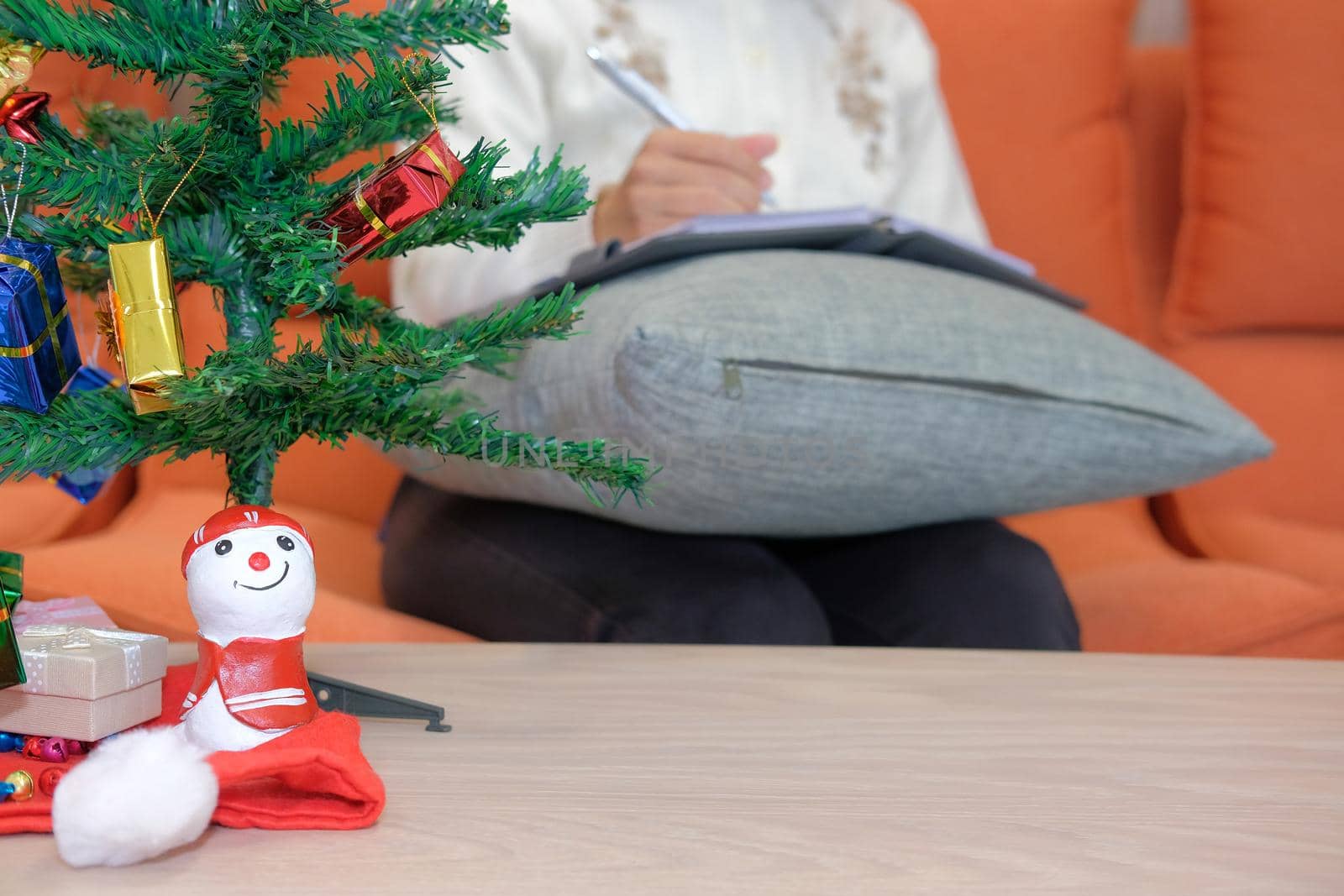 woman wearing cream cardigan writing note on notebook at home with gift present box christmas tree on table. xmas new year celebration.