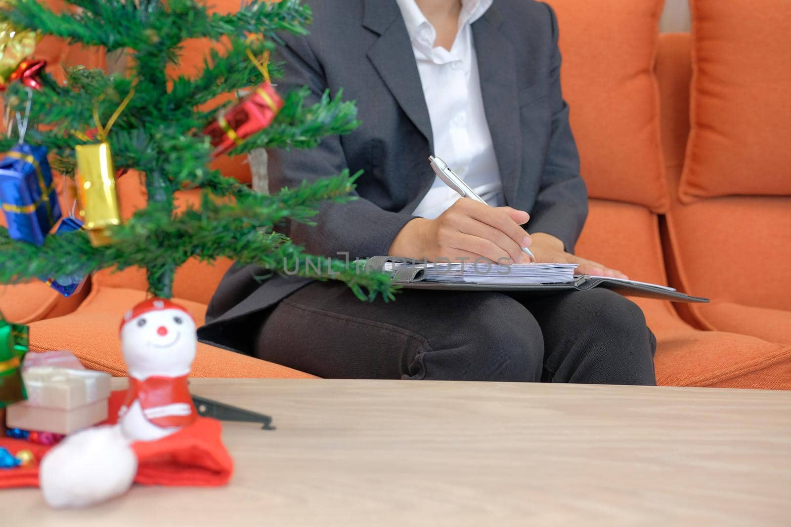 woman wearing suit writing note on notebook with gift present box christmas tree on table. xmas new year celebration.