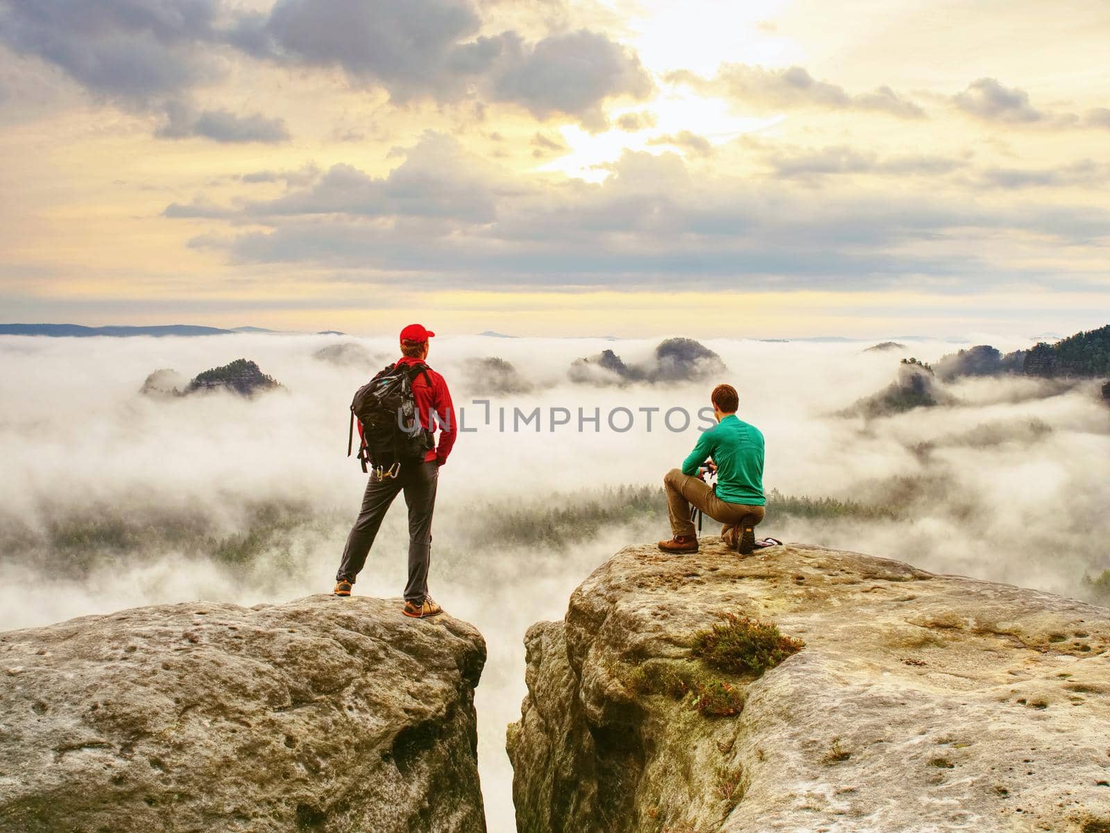 Two friends, hiker thinking and photo enthusiast takes photos of fall landscape. Cold and  mist weather.  Dreamy fogy landscape blue misty sunrise in a beautiful valley below