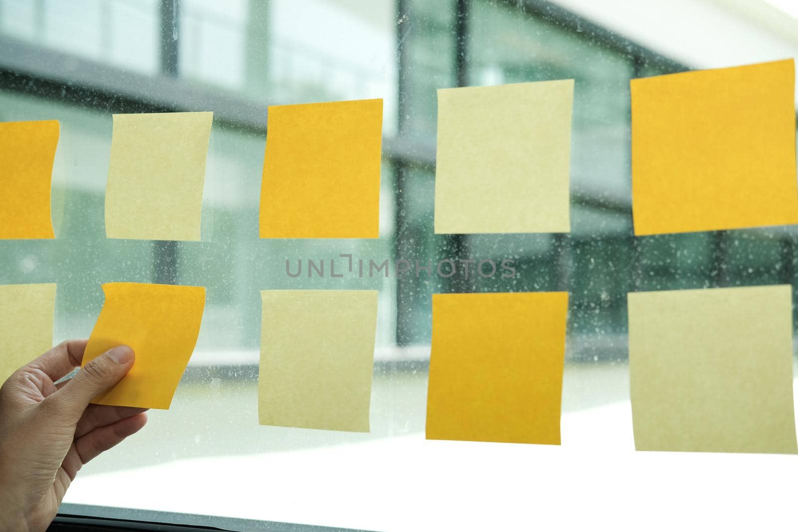 hand hold adhesive notes on glass wall at workplace. Sticky note paper reminder schedule for creative idea & business brainstorming