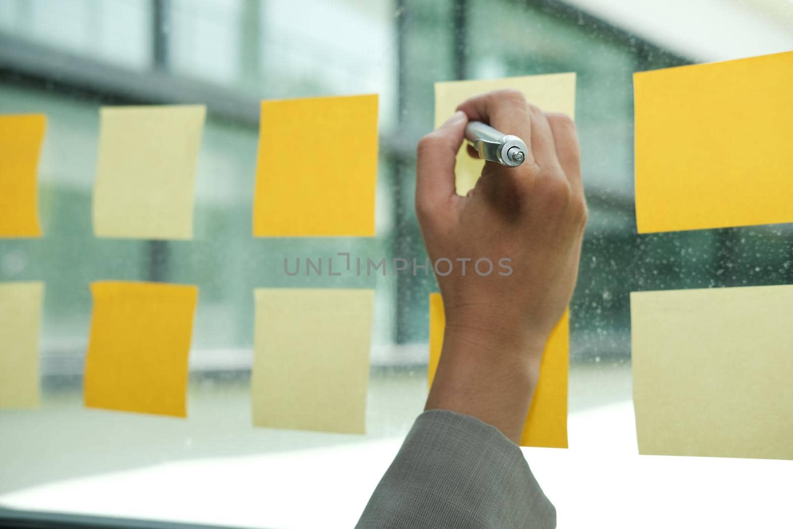 Businessman write on adhesive notes on glass wall at workplace. Sticky note paper reminder schedule for discussing creative idea & business brainstorming