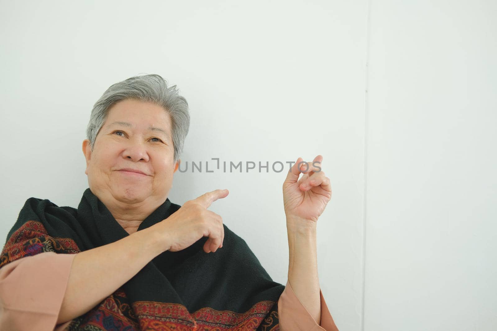 happy old asian elderly elder senior woman pointing up near white wall