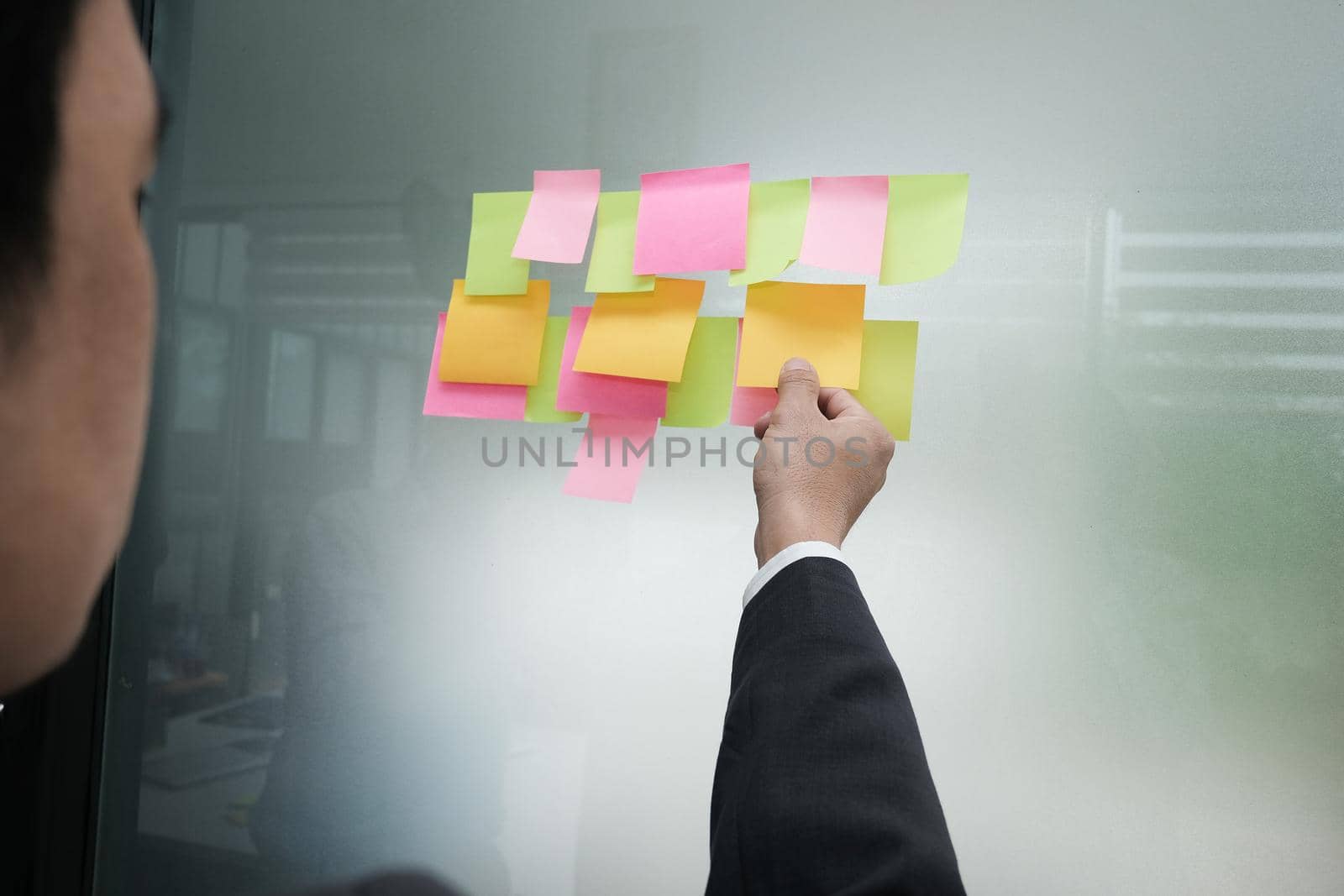 Businessman hold adhesive notes on glass wall at workplace. Sticky note paper reminder schedule for discussing creative idea & business brainstorming