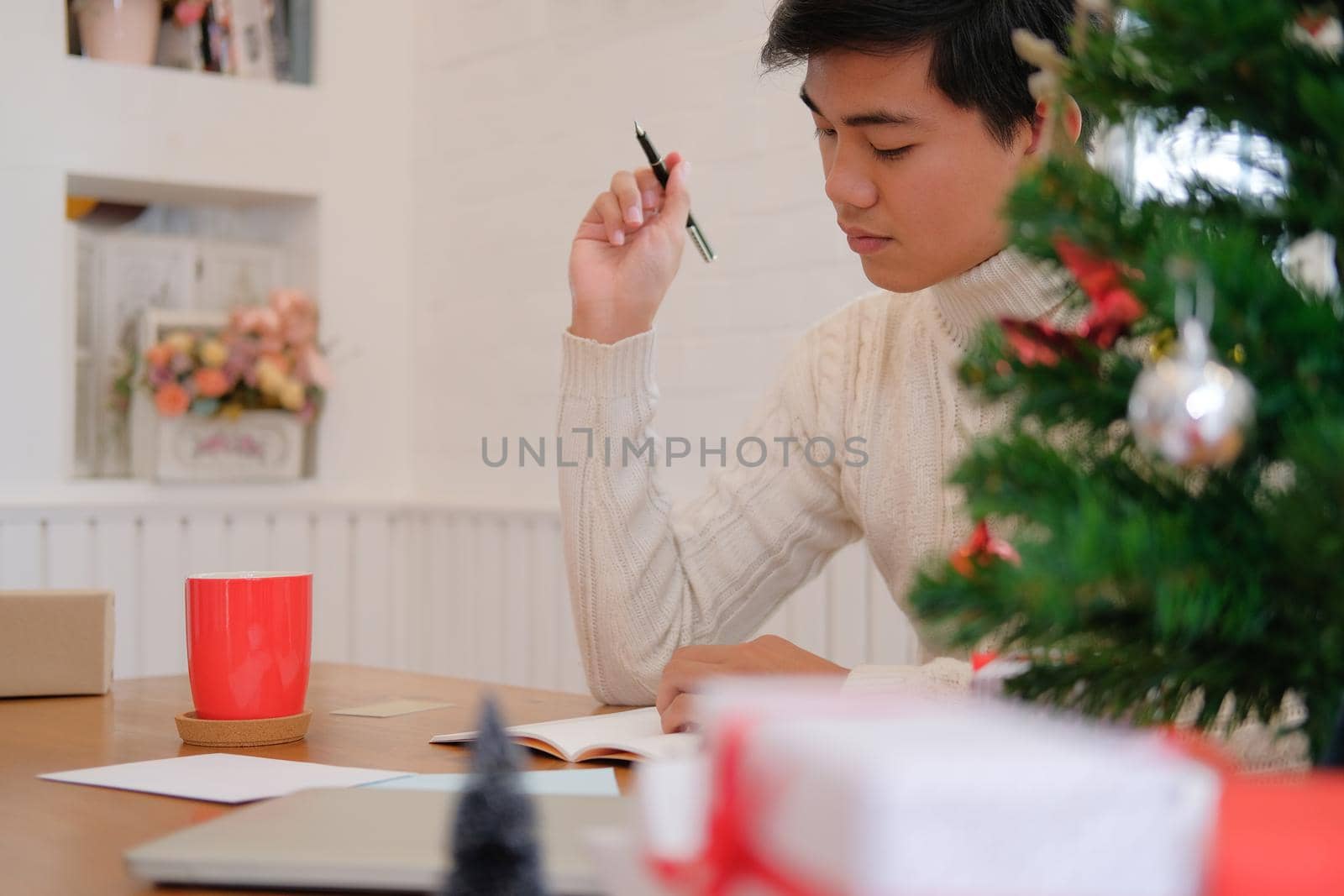 man wearing cream sweater writing note on notebook at home during christmas new year holiday celebration.