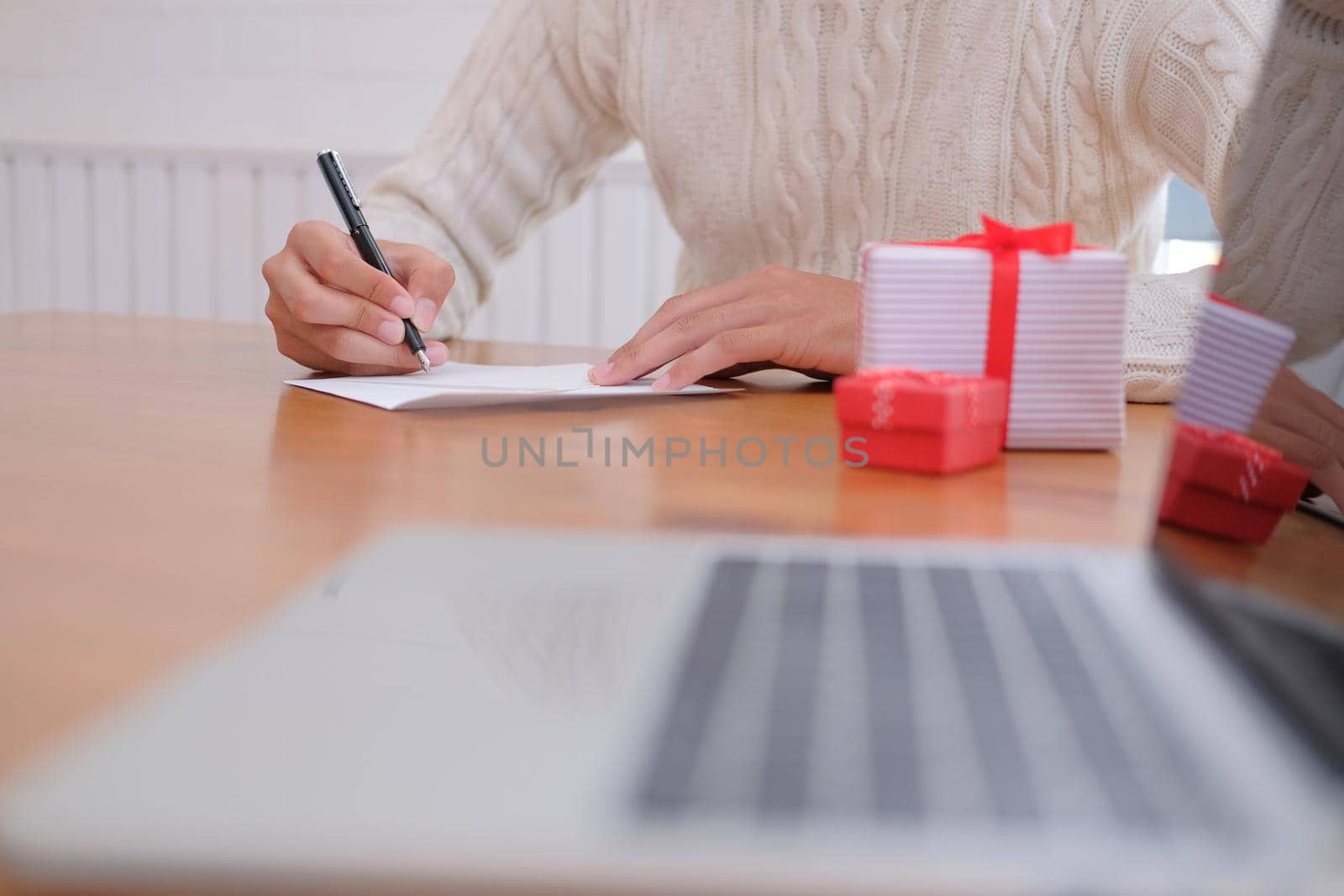 man wearing cream sweater writing christmas letter greeting card holiday wishes with xmas decoration.